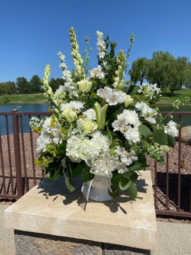 Peaceful Clouds Bouquet - Fluffy white blooms of hydrangea, chrysanthemums, roses, &amp; alstroemeria are paired with greenery in a tall urn style container that works perfectly for Cemetery protocol. Tall and one sided, this arrangement makes a beautiful design for a memorial service. Color customization can be done at no extra charge.  