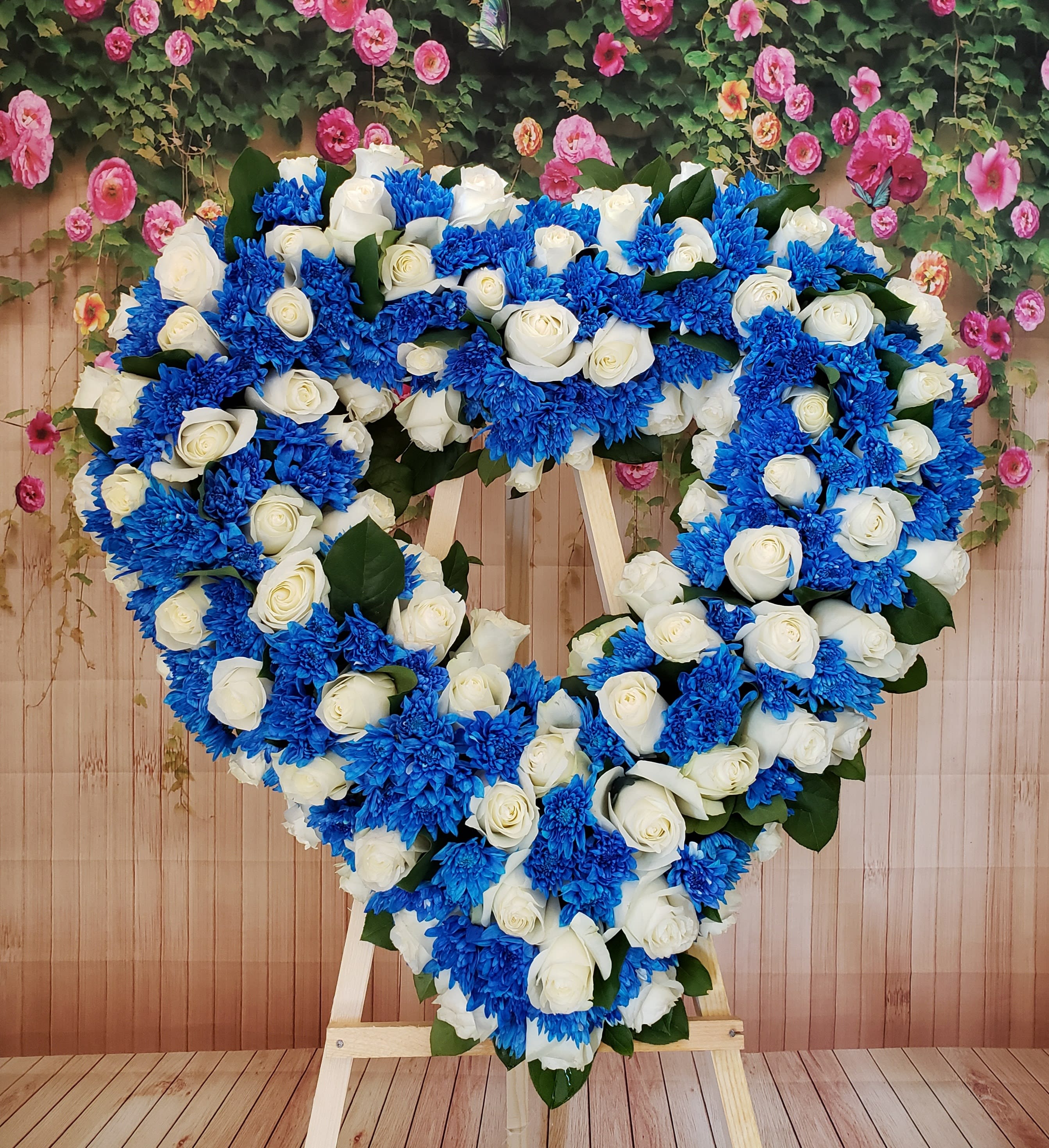 Heart-shaped floral wreath of white roses and blue chrysanthemums on an easel