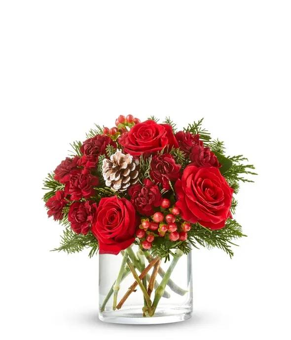 Red roses and carnations in a clear glass vase with pinecones and berries