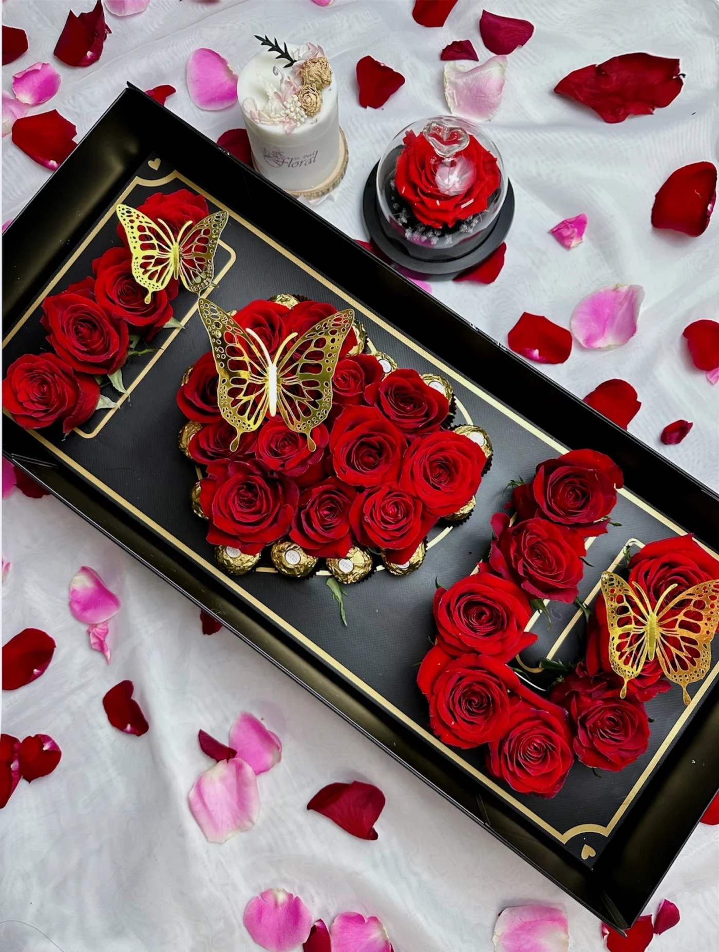 Red roses arranged in a black gift box with gold butterfly accents