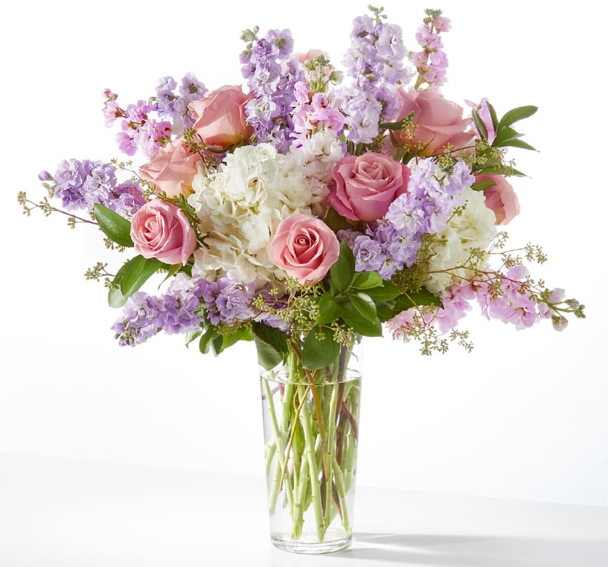 Tall glass vase of pink roses, white hydrangeas, and lavender stock flowers