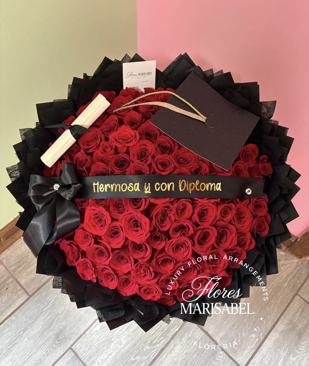 Hermosa y con Diploma - 100 red roses, includes ribbon phrase, cap and diploma. Layered black wrap. 