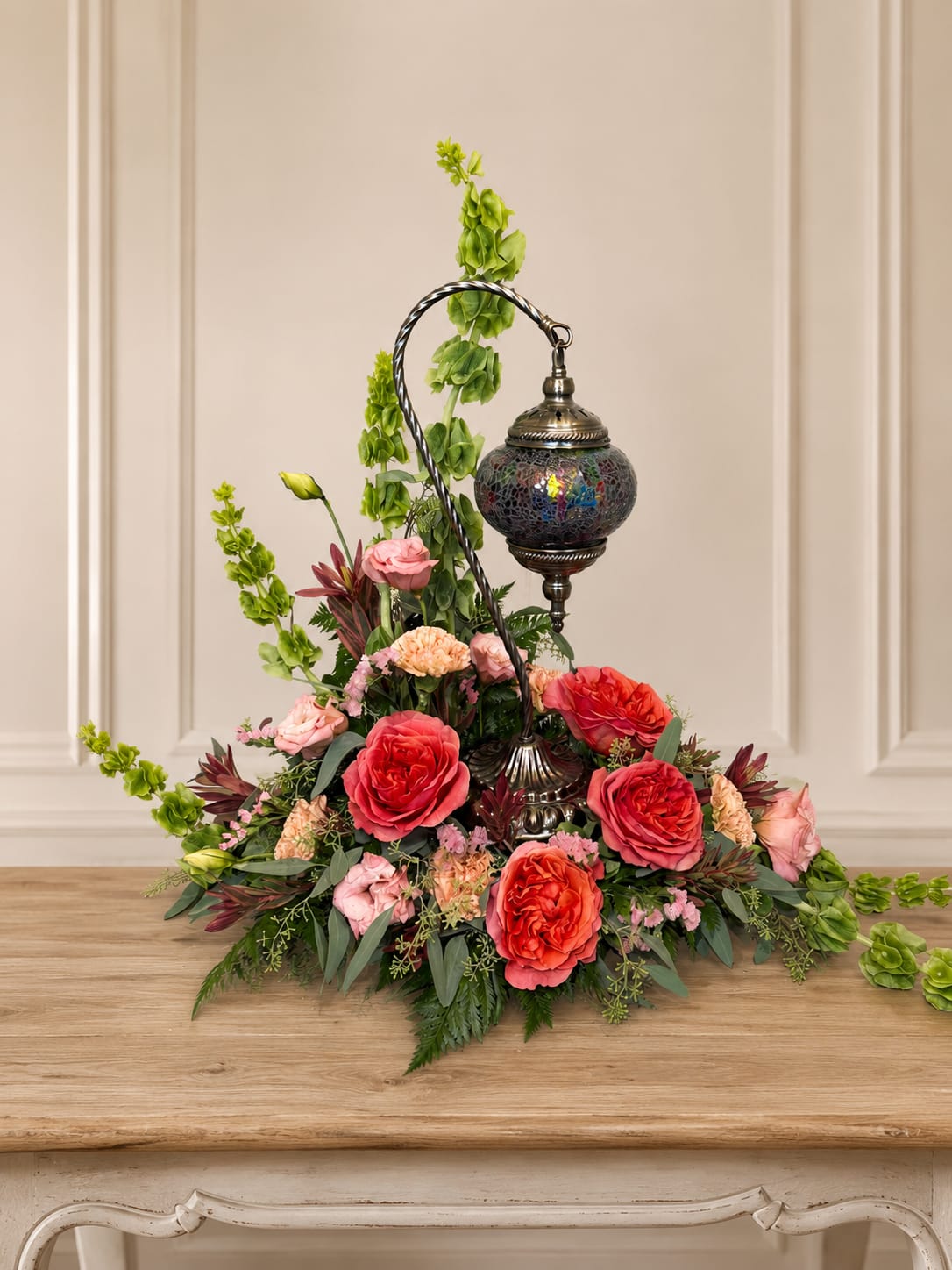 Mosaic Garden Tribute - Bring warmth, beauty, and a touch of elegance to any space with our Mosaic Lantern Garden Tribute. This unique design features a stunning mosaic lantern nestled among lush seasonal blooms and premium greenery, creating a captivating display that serves as both a floral arrangement and keepsake décor piece. Rich coral roses, soft pink accents, textural blooms, and graceful greenery surround the lantern, creating a beautiful balance of color and charm. Perfect for sympathy gifts, memorial services, celebrations of life, or as a meaningful decorative centerpiece.  Please note: Flower varieties and colors may vary based on seasonal availability. Any substitutions will be made with blooms of equal or greater value while maintaining the overall style, color palette, and beauty of the arrangement. Standard Size Shown. Lantern style may vary based on availability.