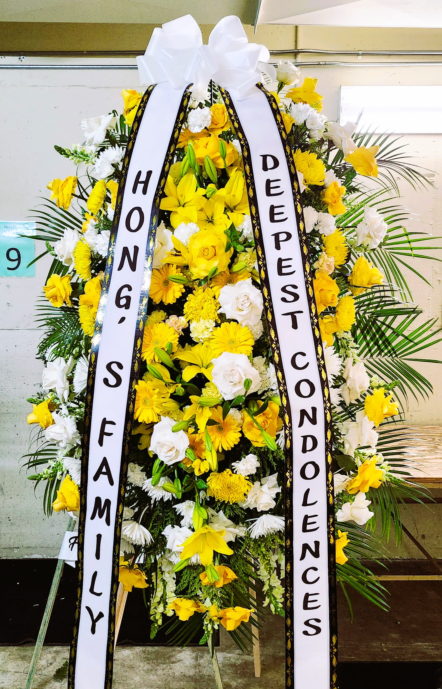 Tall yellow and white standing funeral spray with condolence ribbons on an easel.
