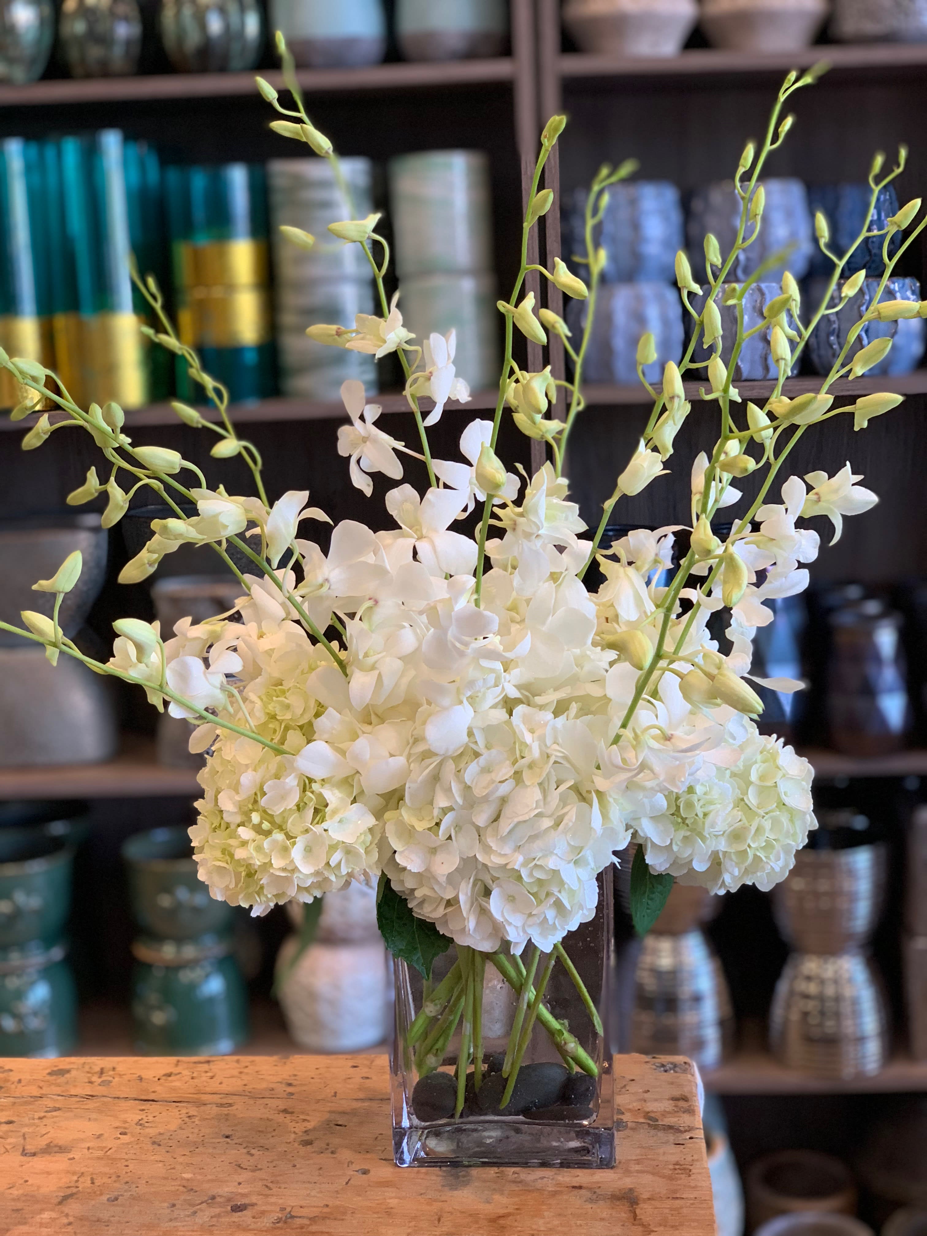 White hydrangeas and orchid stems in a clear glass vase