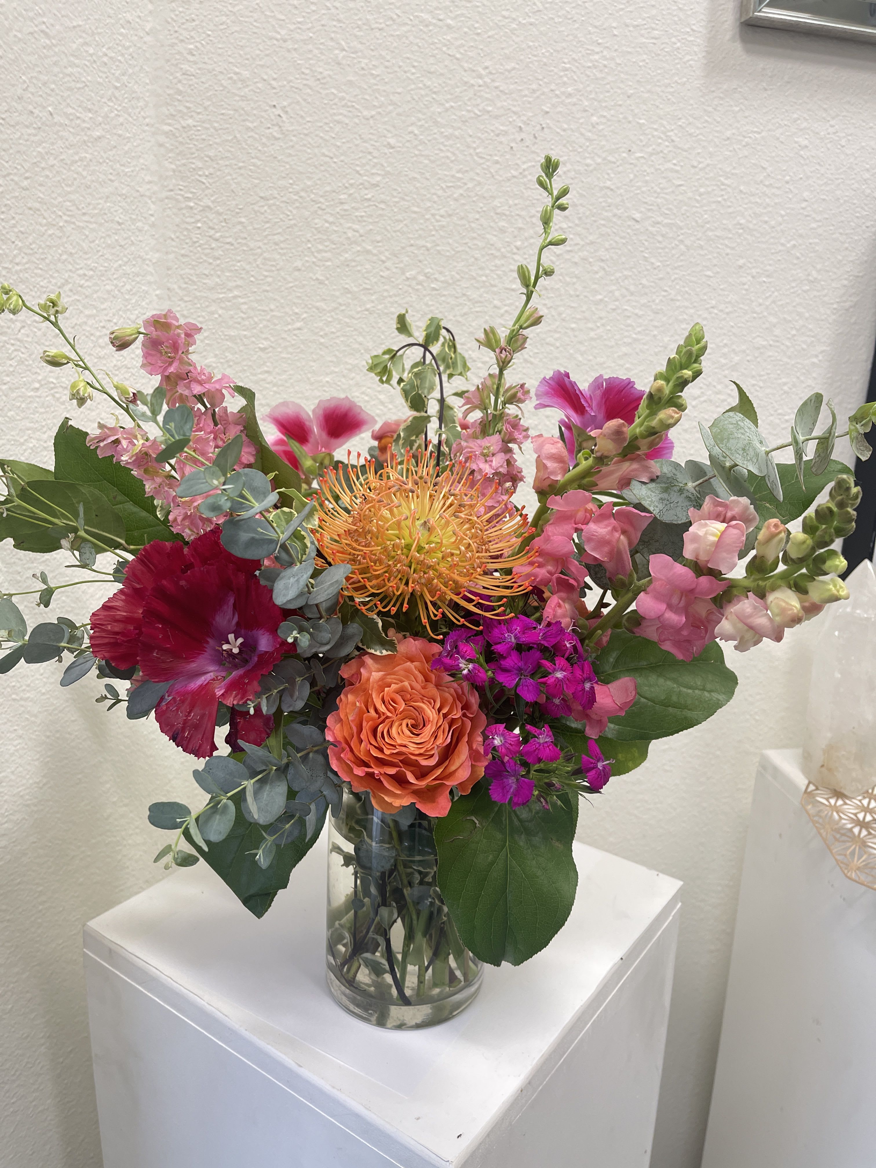 Bright mixed arrangement of orange and pink blooms in a clear glass vase