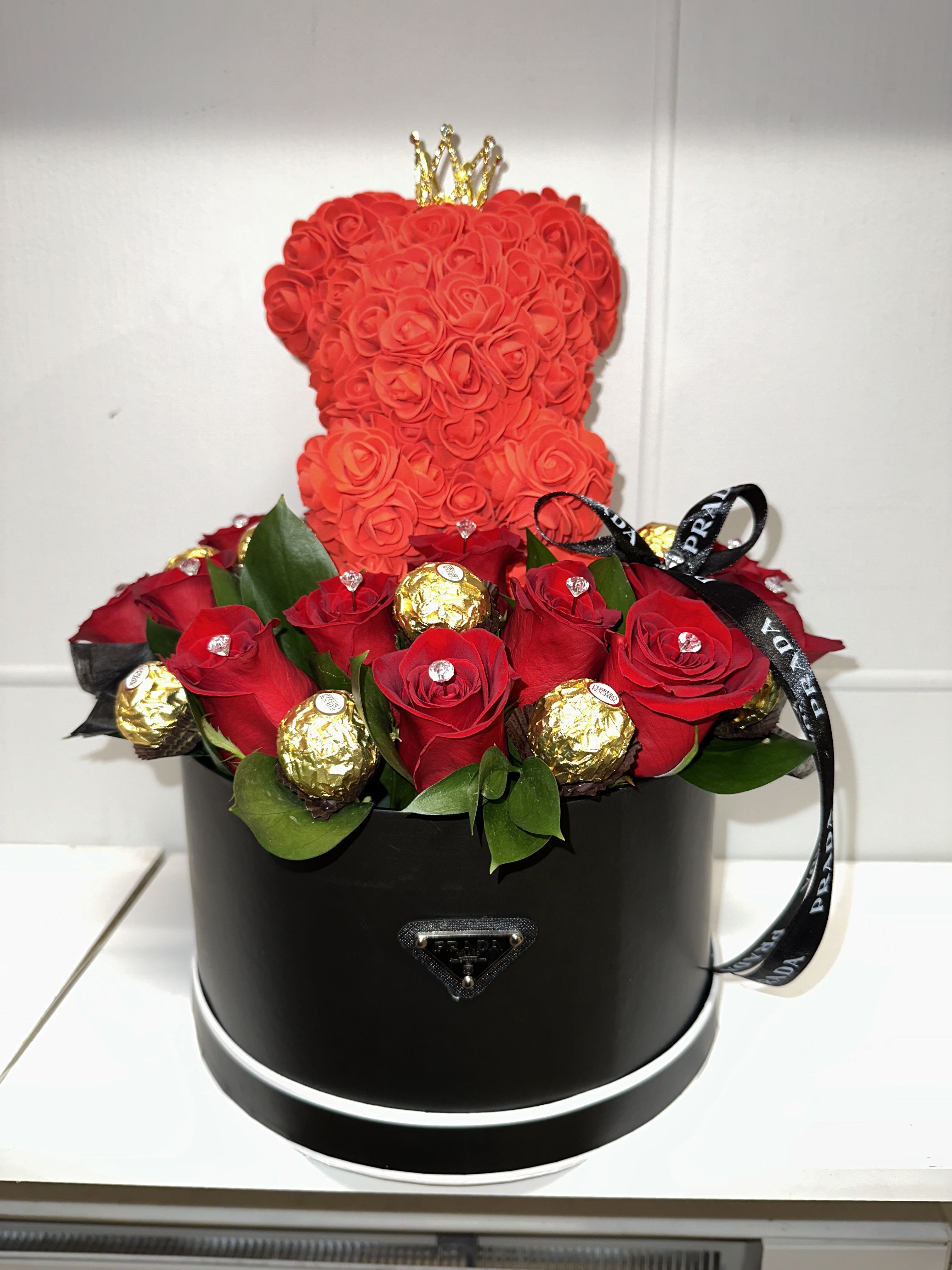 Red rose arrangement in a black round box with a small crown topper