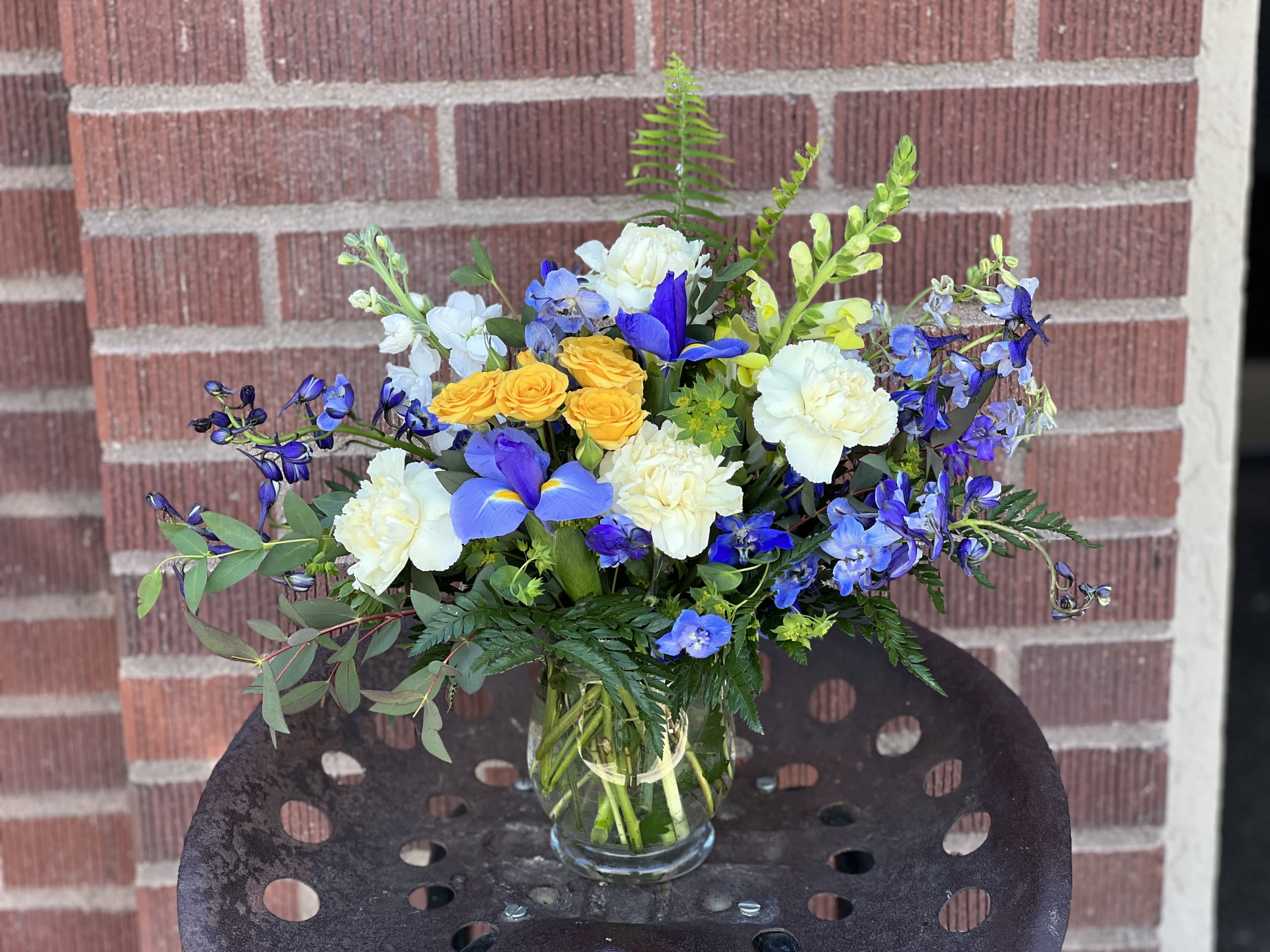 Mixed bouquet of blue, white, and yellow flowers in a glass vase