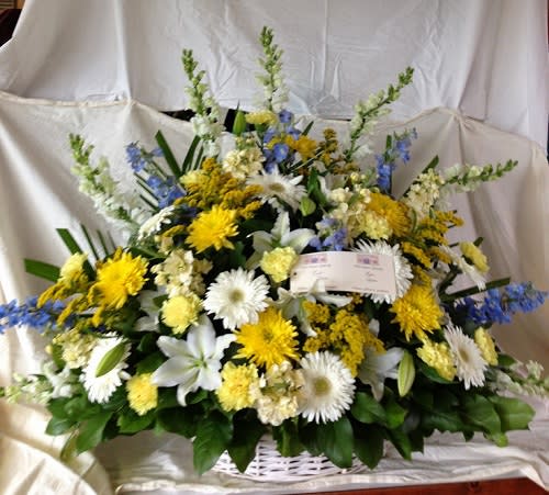 Large mixed floral arrangement in a white basket with yellow, white, and blue blooms