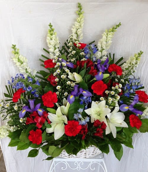 Large mixed flower arrangement in a white basket with red, white, and purple blooms