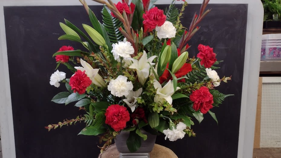 Devotion and Grace - A striking sympathy arrangement featuring red and white blooms, graceful lilies, and lush greenery. Designed to honor a cherished life with love, remembrance, and heartfelt compassion.