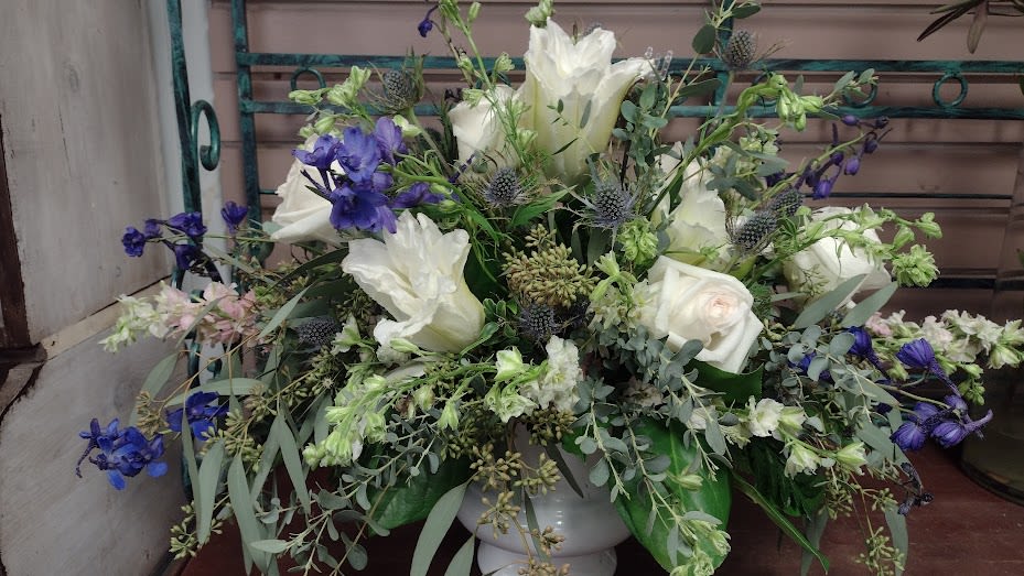Whispering Meadows - A garden-inspired arrangement featuring white blooms, blue delphinium, thistle, and lush greenery