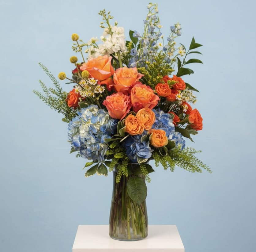 Amalfi Coast Escape - Inspired by the vibrant colors of the Italian coastline, Amalfi Coast Escape combines stunning blue hydrangea, coral roses, spray roses, airy delphinium, and seasonal garden accents in a lush, elevated design. Reminiscent of seaside sunsets and Mediterranean gardens, this cheerful arrangement is full of texture, movement, and color. Perfect for celebrations, birthdays, thank you's, or bringing a little vacation feeling home.