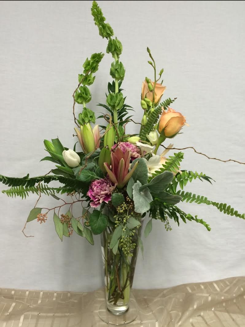 Tall mixed floral arrangement in a clear glass vase with peach roses and pink blooms