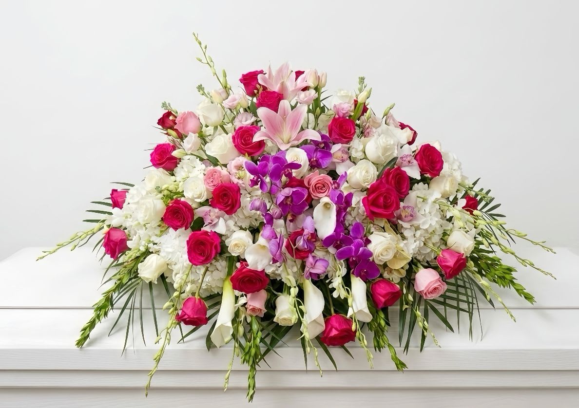 Loving Memories Casket cover - A grand and comforting horizontal casket spray designed to beautifully honor a cherished life. This premium, multi-dimensional tribute features an abundance of vibrant hot pink, soft blush, and pristine white roses, elegantly intermingled with striking pink lilies, majestic purple orchids, and crisp white calla lilies. Grounded in a luxurious bed of fluffy white hydrangeas and accented with premium flowing greenery, this exquisite arrangement brings unparalleled grace, dignity, and a profound sense of peace to the memorial service.
