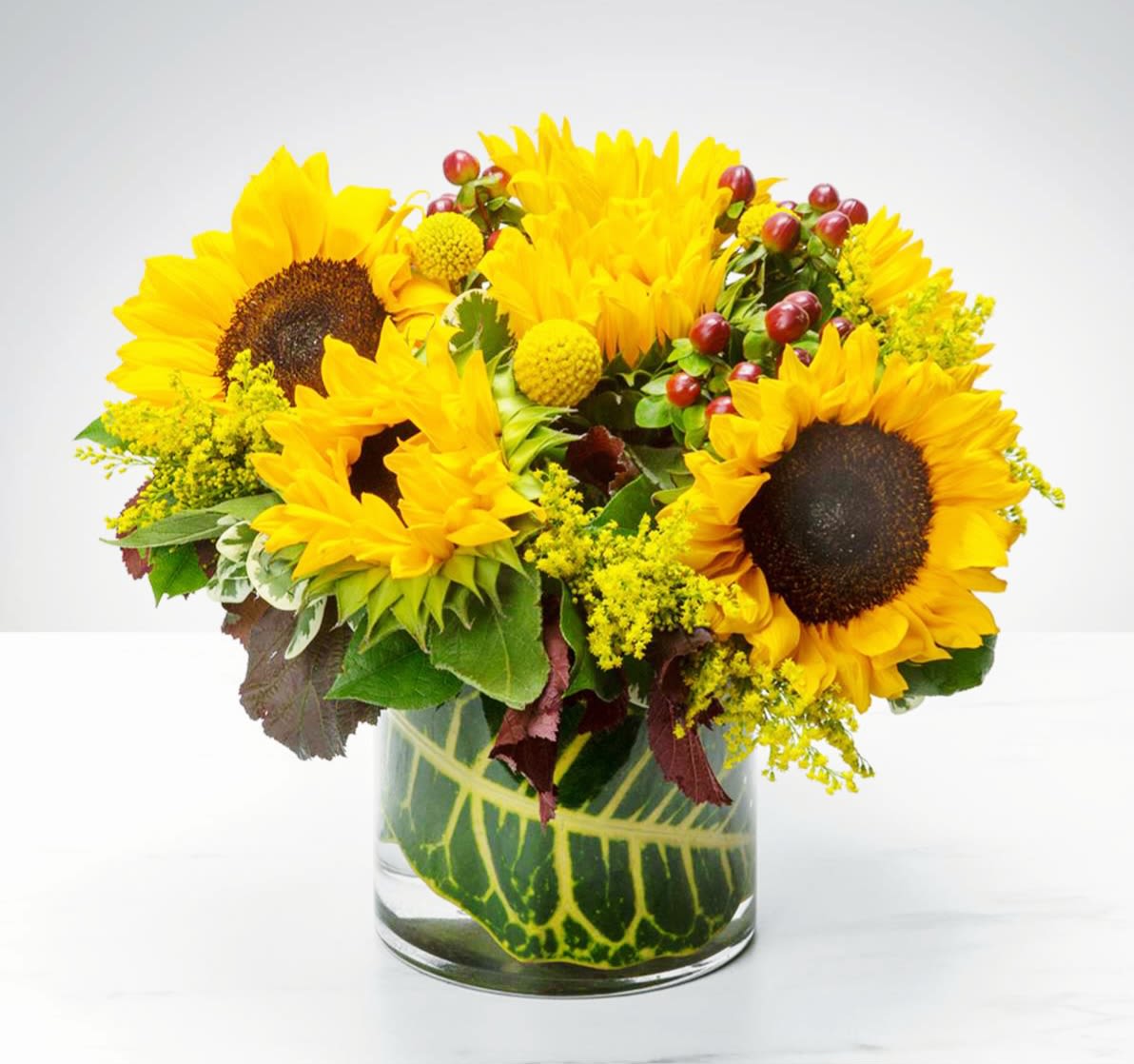 Sunflower arrangement in a clear glass vase with yellow filler flowers