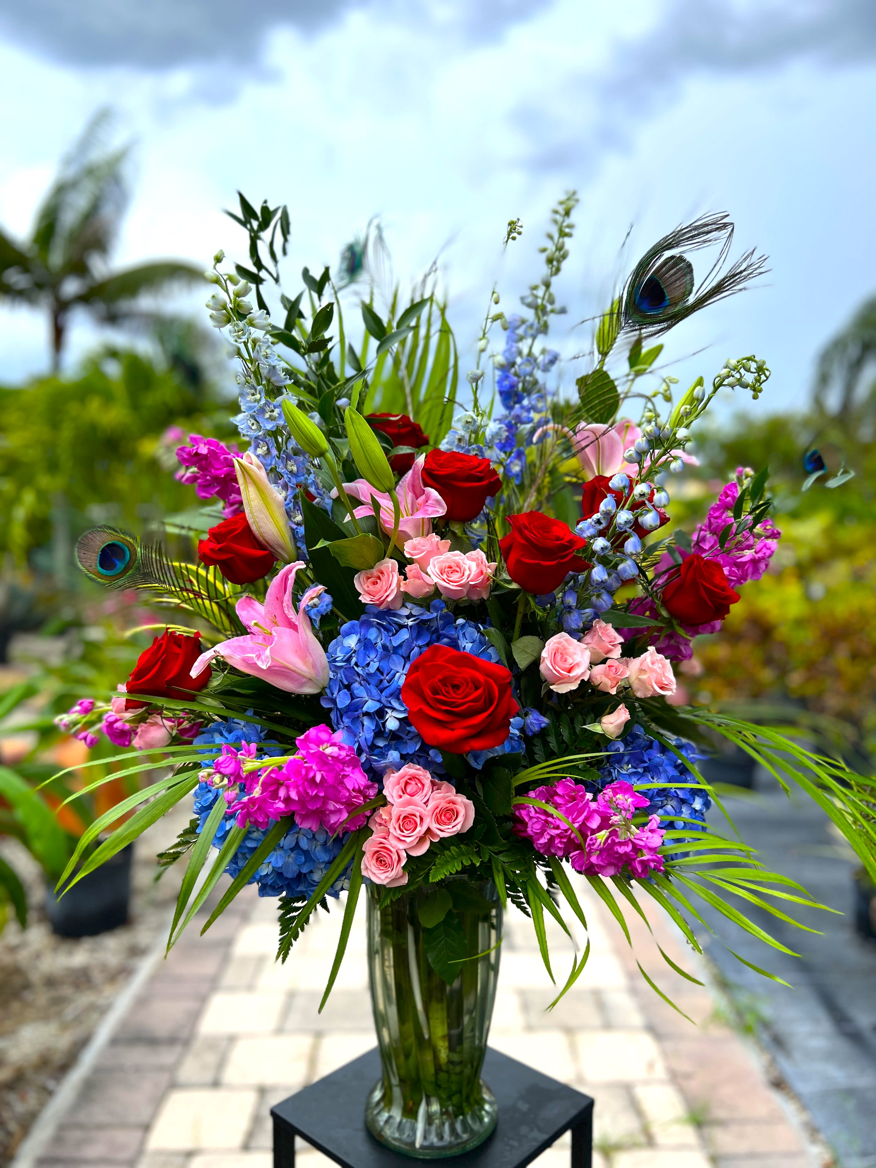 Tall bouquet of red roses, pink lilies, blue hydrangeas, and purple flowers in a glass vase