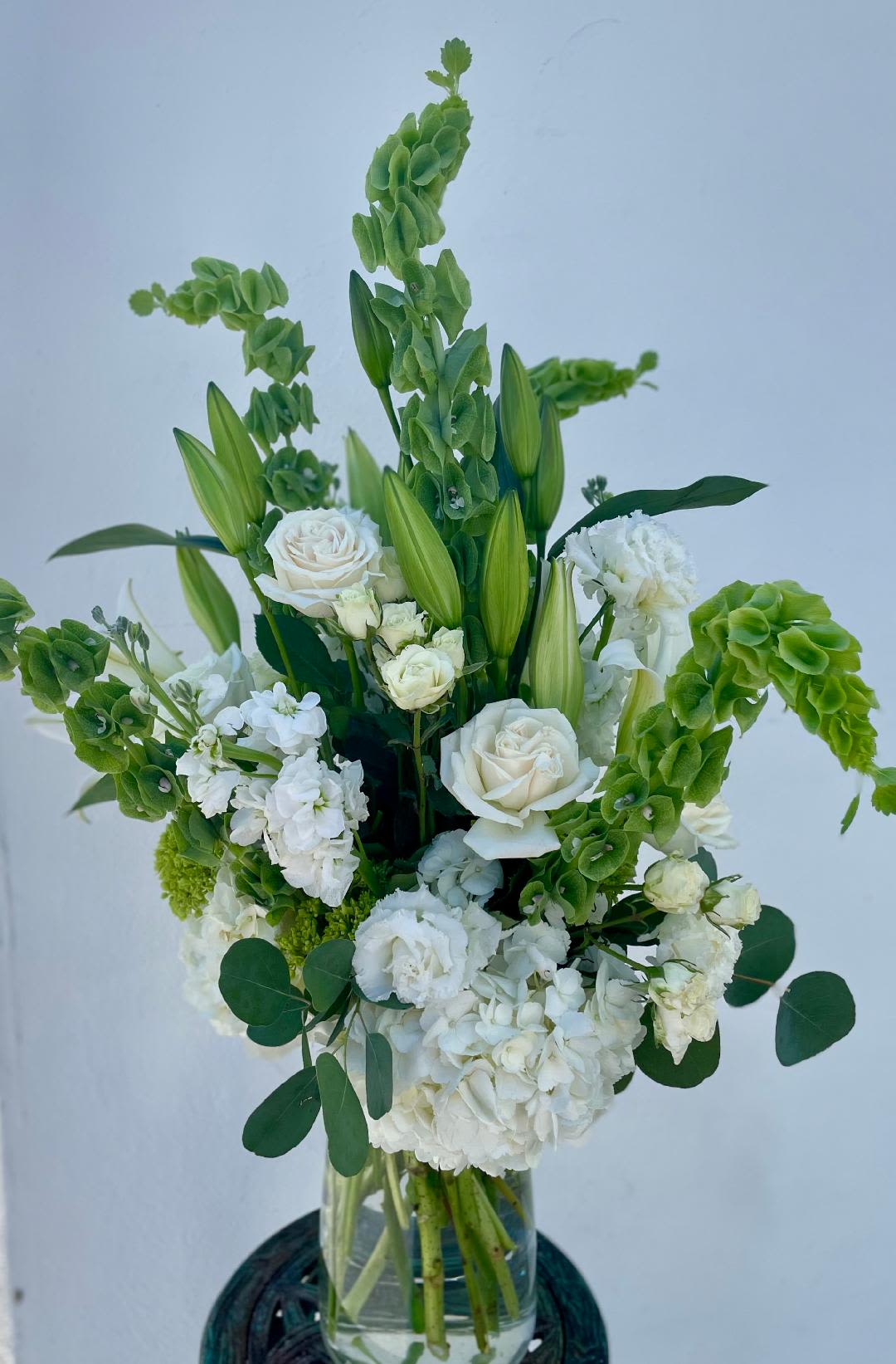 CFS117 - A tall showy white and green vased arrangement with flowers such as lilies, roses, hydrangea, bells of ireland and other high end blooms. 