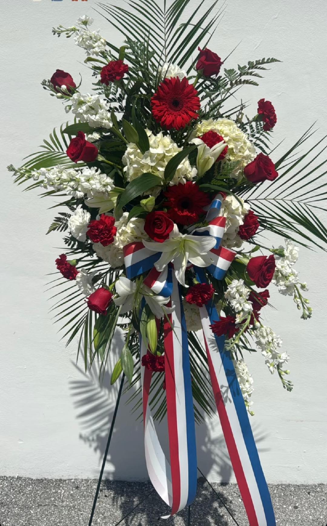 CFS102 - A standing spray for a funeral service in red, white and blue flowers such as roses, lilies, hydrangeas, stock, gerber daises, carnations and other blooms. 