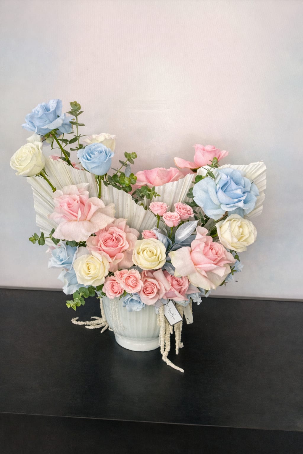 Pastel roses arranged in a white vase with pleated paper accents