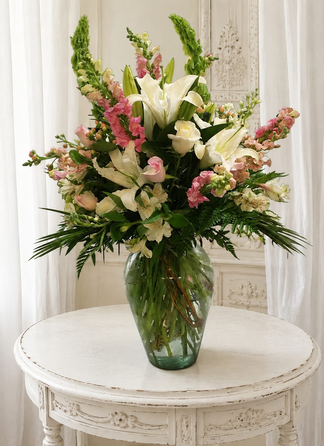 Pink and white delight - Tall, abundant white lilies crown this Pink and white delight flower arrangement, giving the bouquet a fragrant, garden-fresh presence perfect for a birthday bouquet, anniversary roses alternative, or romantic surprise. The upright spikes of pink snapdragons pair with soft blush alstroemeria and pale pink roses to create a full, airy silhouette that feels both celebratory and refined - the kind of gift that makes the person you're thinking of feel truly cherished.  Set in a clear glass vase, the design balances vertical movement from the snapdragons with broader, layered textures from the lilies, alstroemeria, and roses. Dark green foliage frames the white and pink palette, enhancing each bloom's color and adding a fresh, elegant contrast suitable for a formal table display or bedside centerpiece. This arrangement arrives ready to display on a dining table or entry console; regular fresh water changes and a cool spot away from direct sun will help the blooms last longer.   If any design elements are of major importance to your order, please include them in the florist instructions at checkout or contact us to ensure availability.