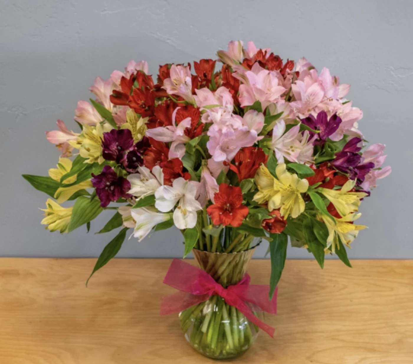 Mixed bouquet of colorful alstroemeria in a glass vase with a pink ribbon
