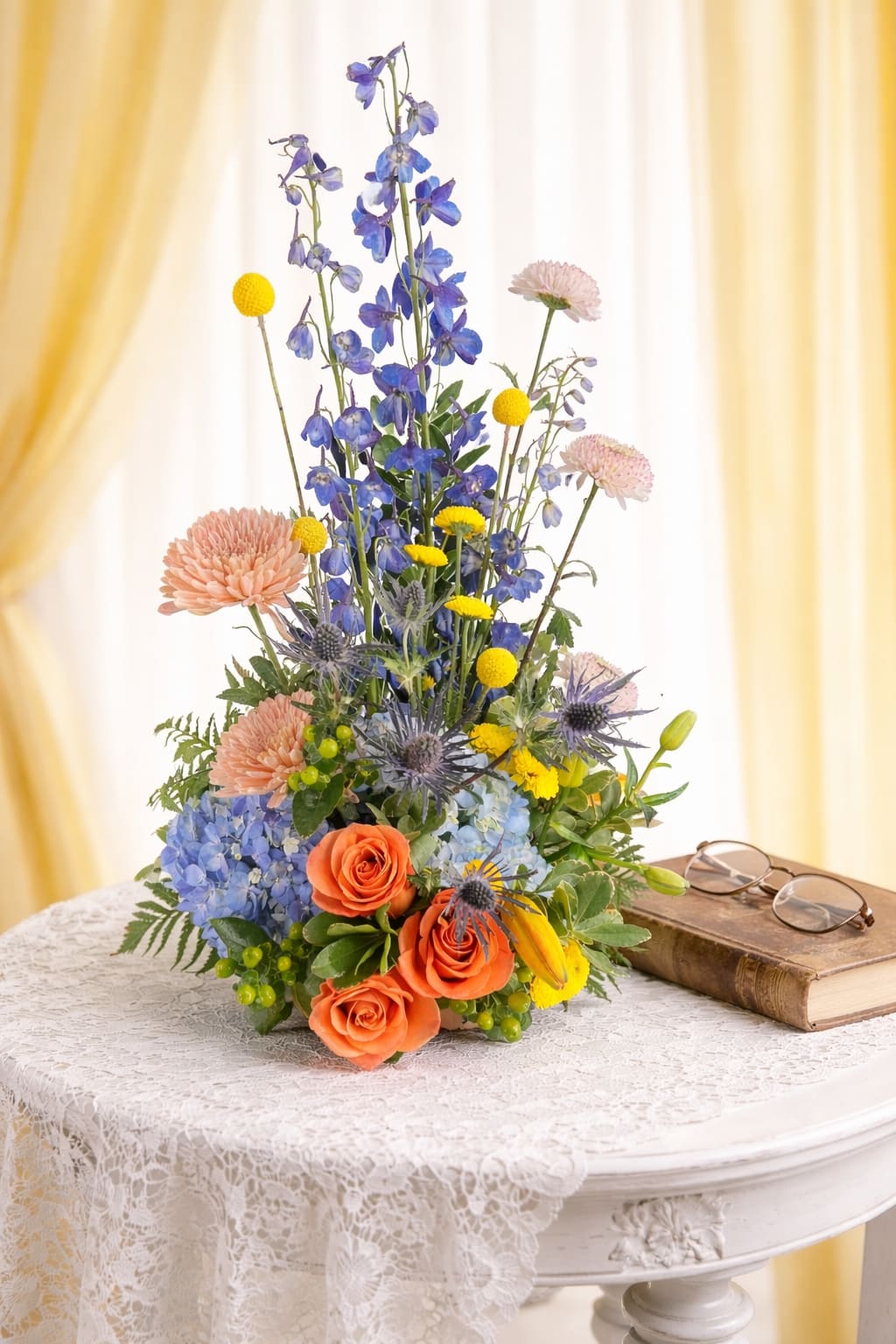 Sky high blue - Sky-high blue delphinium gives this tall mixed bouquet an immediately striking, garden-fresh presence-perfect as a cheerful birthday bouquet or an anniversary surprise. The vertical lines of the delphinium reach above a plush base of peach roses and blue hydrangea, so the person you're gifting will see both drama and intimacy in one arrangement.  At the base, soft round roses and voluminous hydrangeas are warmed by small yellow accent blooms and orange-toned chrysanthemums, while spiky thistle-like flowers add texture and contrast against the smoother petals. The palette of cool blues with peach, orange, and yellow creates a lively, romantic look that feels airy and abundant.  This bouquet works well for celebrating milestones, brightening someone's home, or saying "I'm thinking of you" with a bit of elegant flair-the recipient will feel genuinely seen and celebrated. The tall, layered design makes a strong focal statement.   If any design elements are of major importance to your order, please include them in the florist instructions at checkout or contact us to ensure availability.