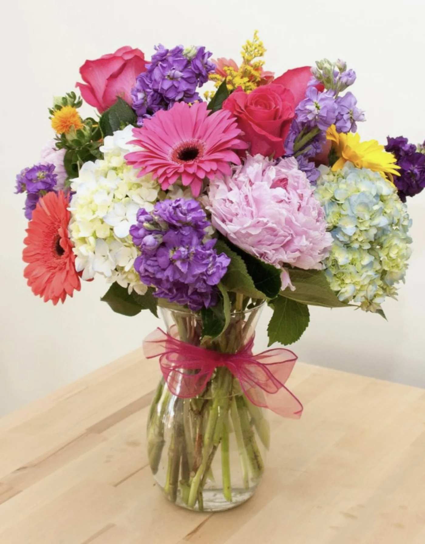Mixed bouquet of pink, purple, yellow, and white flowers in a glass vase
