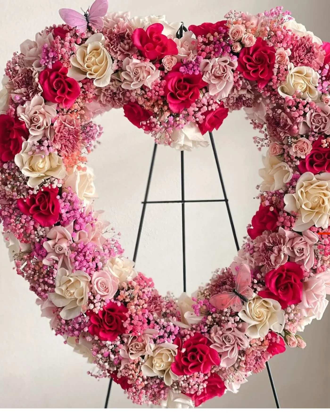 Heart-shaped floral wreath with pink and cream roses on a stand