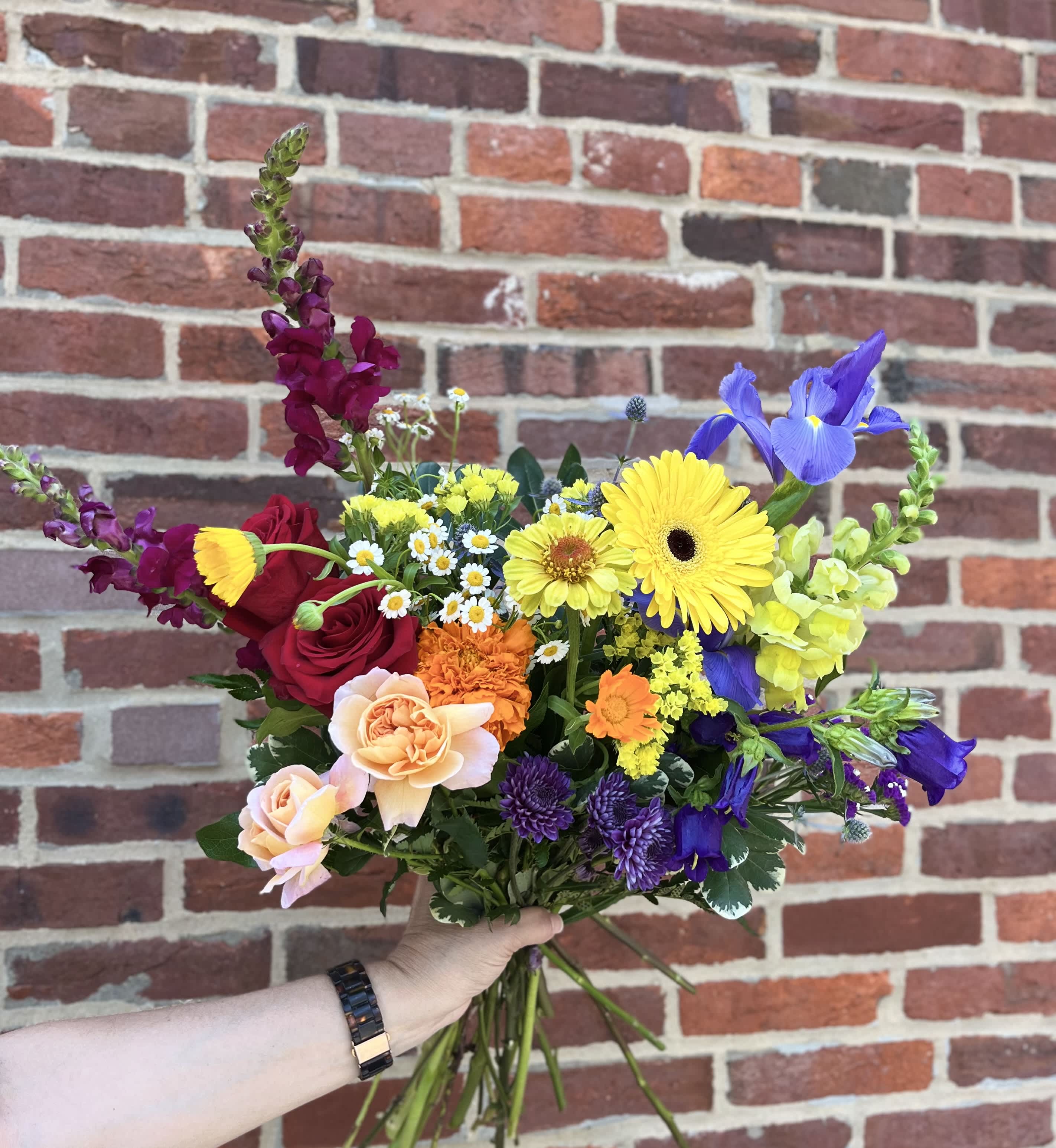 Colorful hand-tied bouquet with yellow gerbera daisies, red roses, purple irises, and assorted mixed flowers
