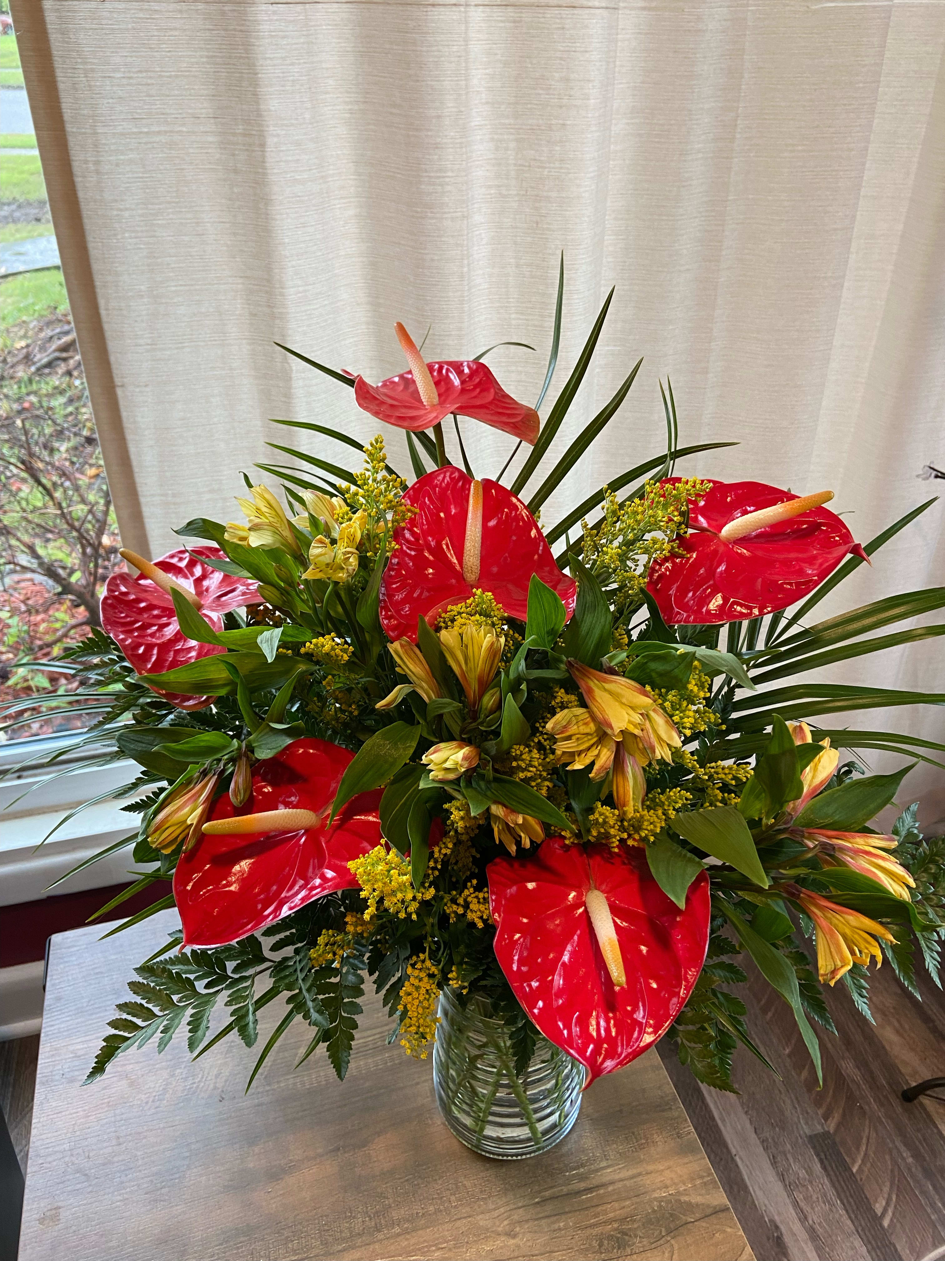 Red anthuriums and yellow flowers in a glass vase
