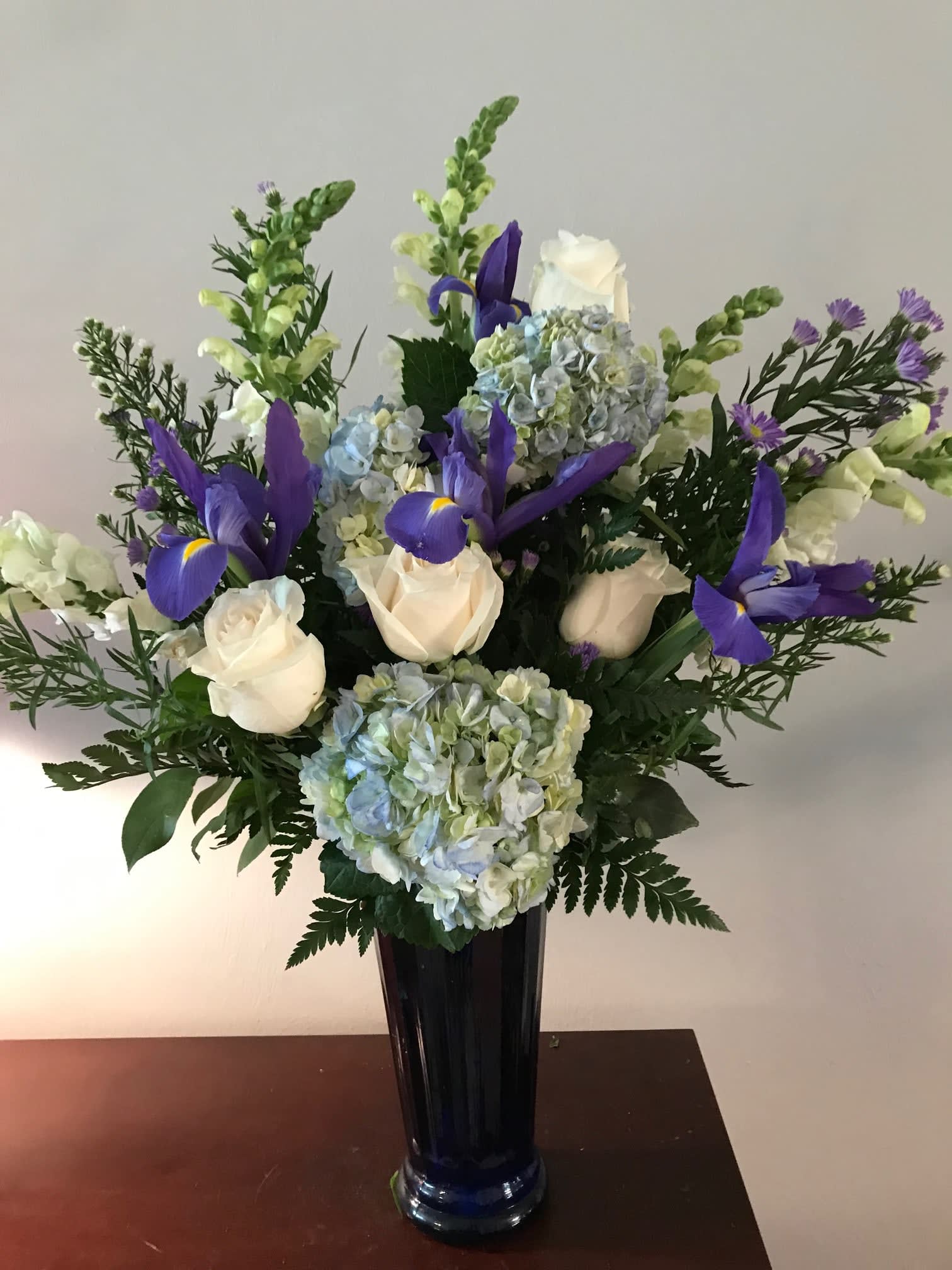 White roses and blue hydrangeas with purple irises in a tall vase