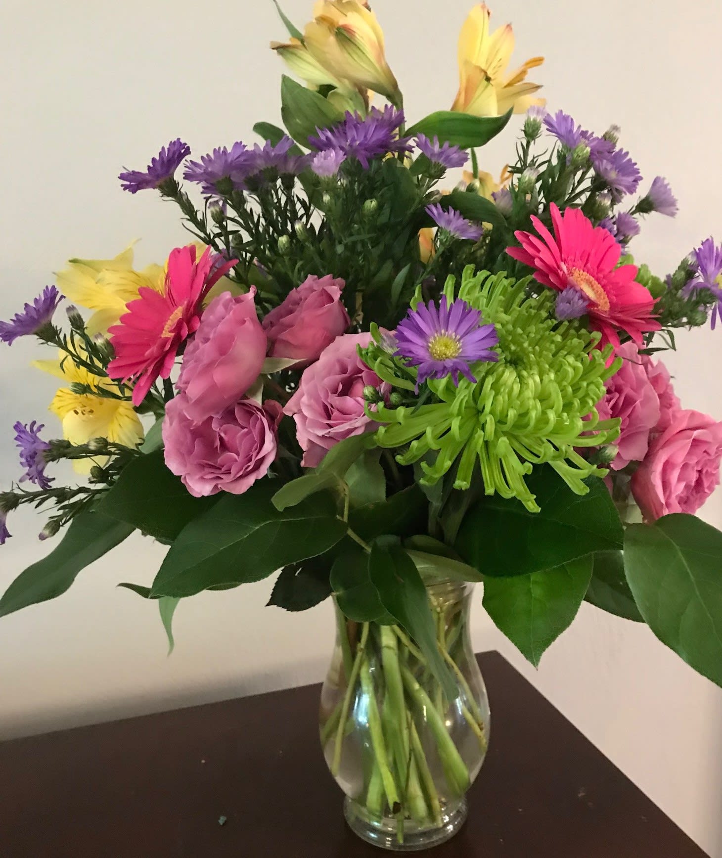 Mixed bouquet of pink roses, gerbera daisies, and purple flowers in a glass vase