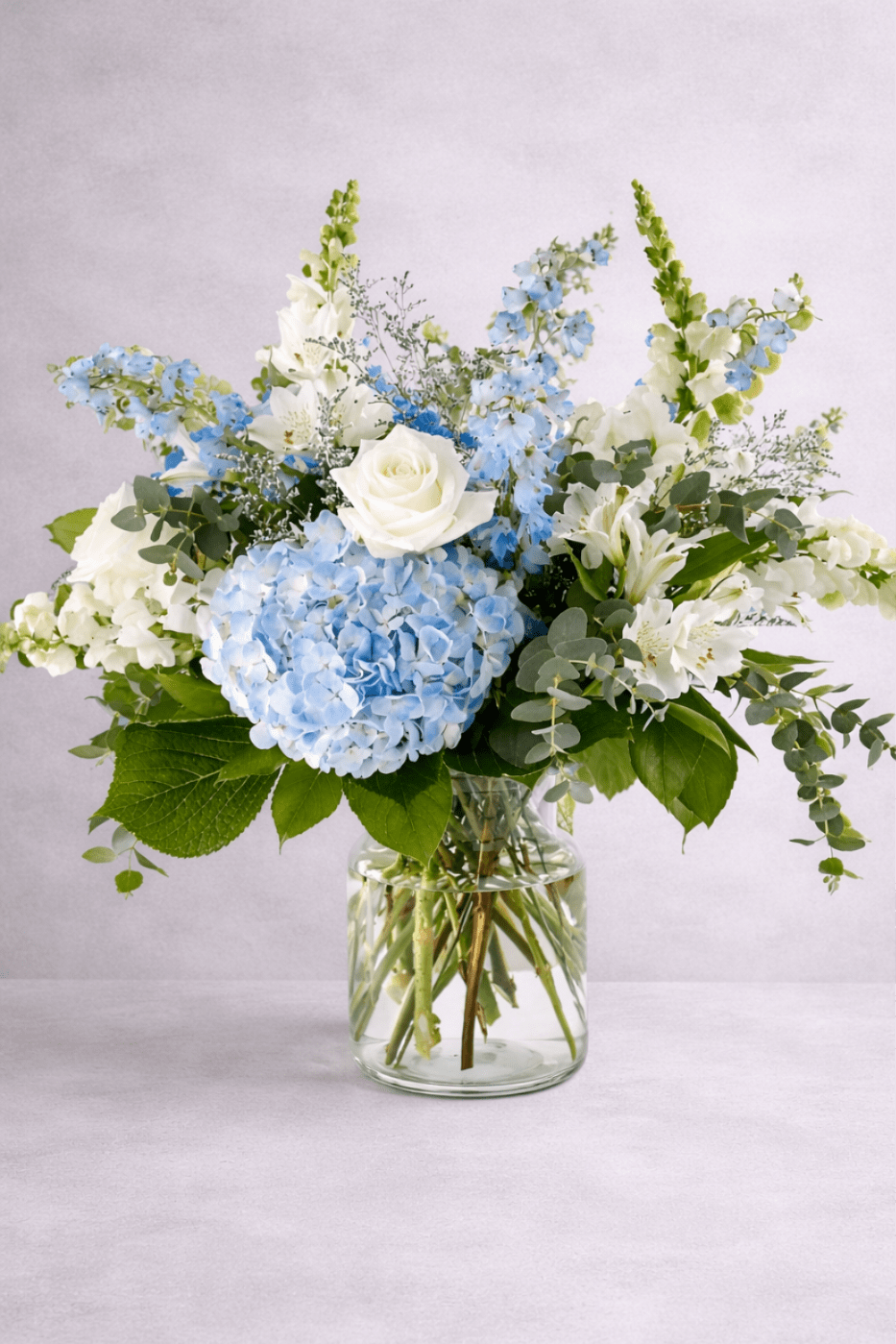 Classic Blue - Bright white and blue hydrangeas, white roses, delphinium and snapdragons create a perfect yet simple Classic Bouquet Arranged beautifully in a glass vase 