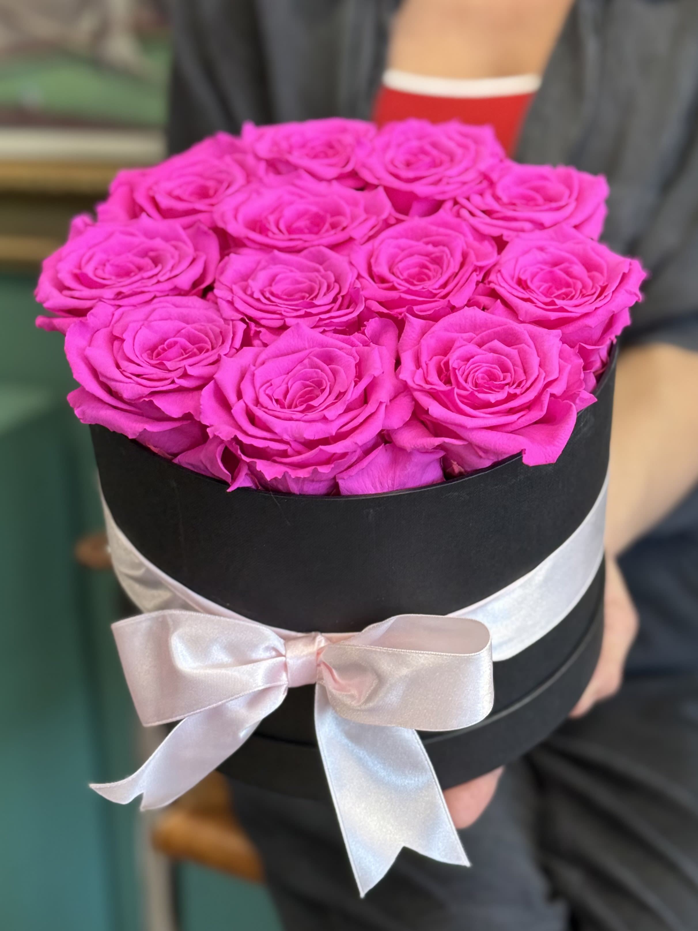 Bright pink roses arranged in a black round box with a pale ribbon bow