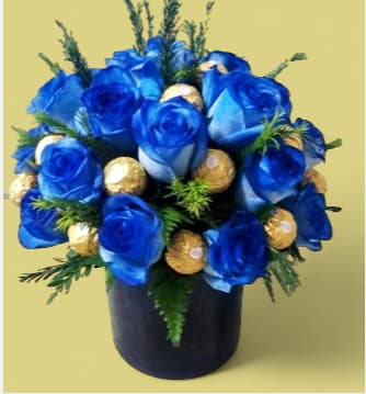 Royal Blue Centerpiece - A high-end, three-dimensional design crafted exclusively for Father's Day. Features a refined selection of deep sapphire blue roses and gourmet Ferrero Rocher chocolates, artistically arranged in a sleek black cylinder with premium seasonal greenery. Ready to elevate his favorite space!