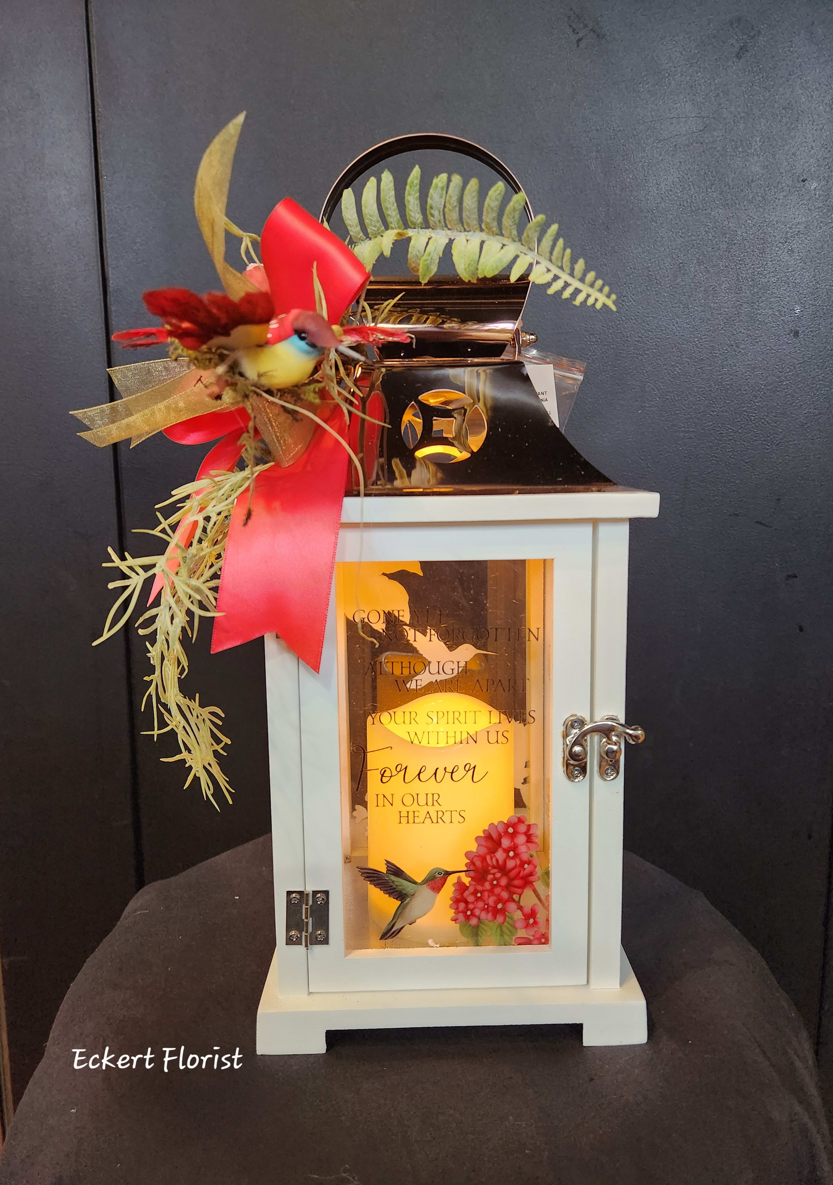 Eckert Florist's "Gone Yet Not Forgotten..." Hummingbird Lantern - Nice keepsake white wooden lantern with Copper tin roof and sentiment on flower and hummingbird motif glass. Sentiment: "Gone yet not forgotten Although we are apart Your spirit lives within us Forever in our hearts." Included is a battery operated candle. Measures approx. 6.25" Square x 15" High *OUR LOCAL DELIVERY ONLY