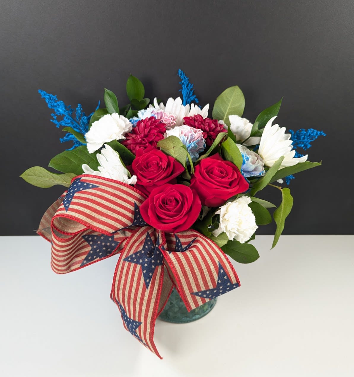 Bouquet of red roses, white daisies, and carnations in a glass vase with patriotic ribbon