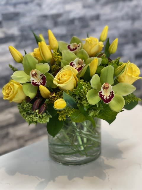 Yellow roses and orchids arranged in a glass vase
