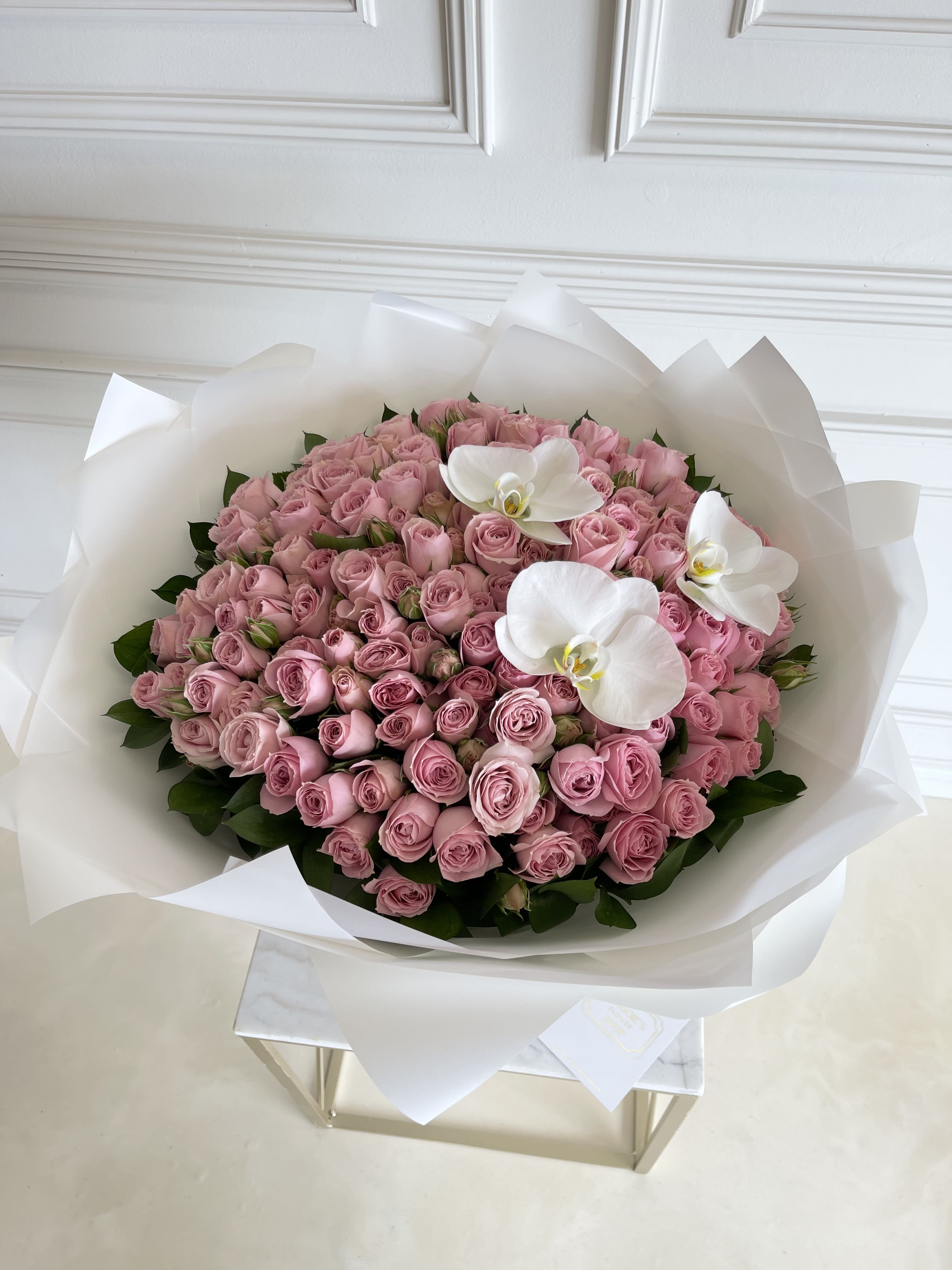 Large bouquet of pink roses with white orchids wrapped in white paper