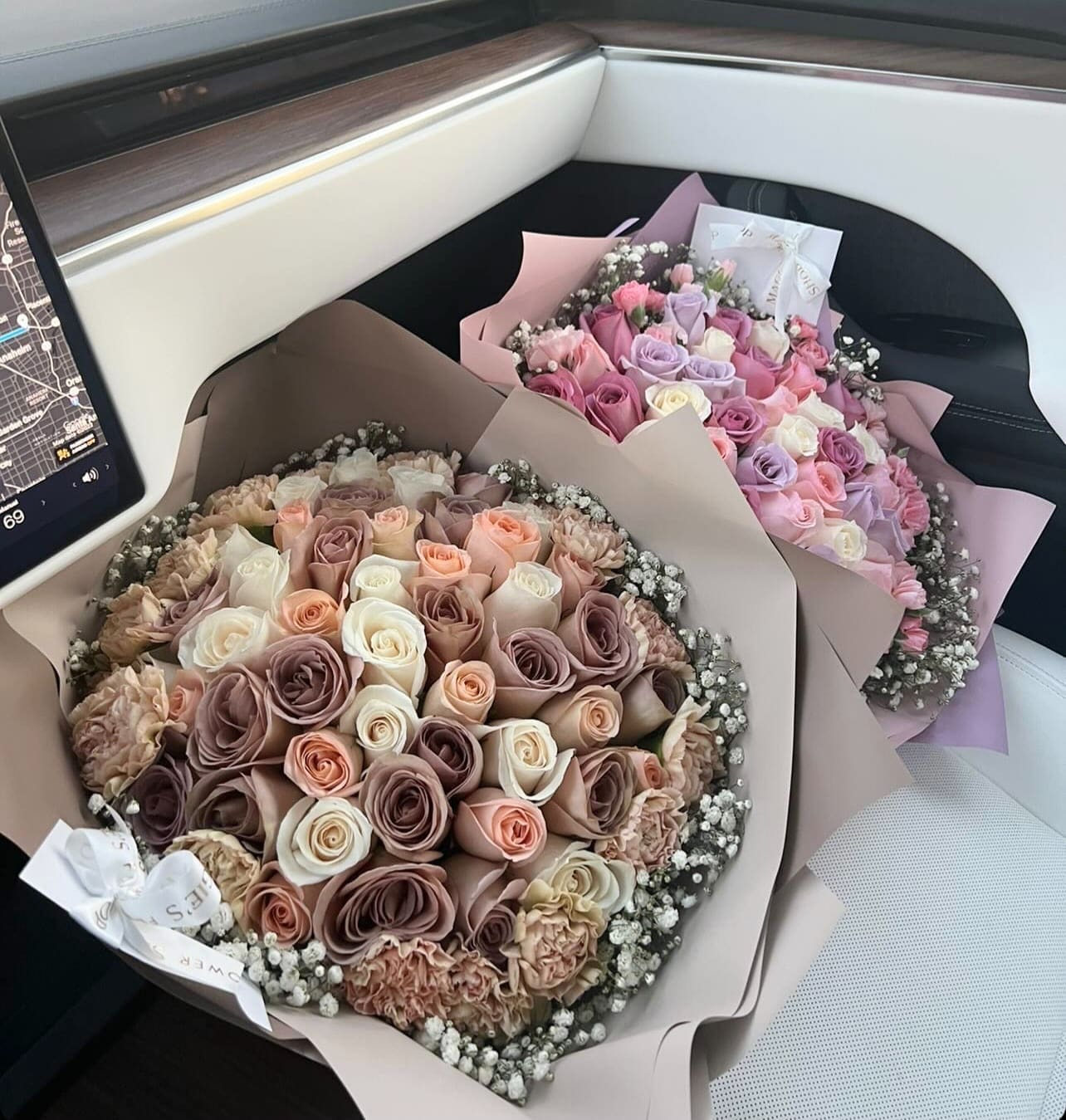 Two bouquets of pastel roses wrapped in paper on a car seat
