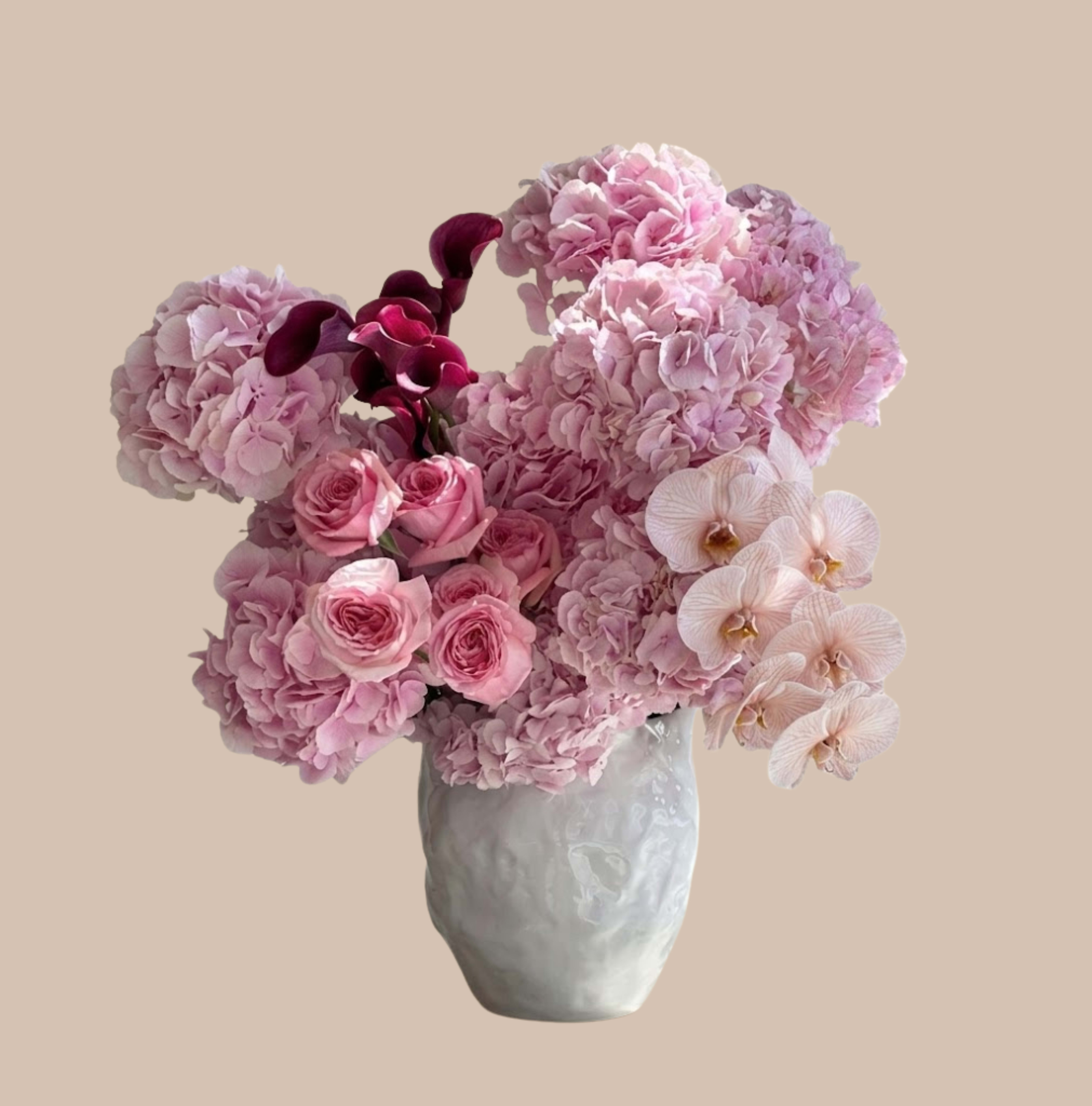 Lace &amp; Labyrinth - Soft pink hydrangeas and blush phalaenopsis orchids mingle with pink roses to create a romantic birthday bouquet or anniversary arrangement that feels both lush and intimate. The addition of deep magenta calla lilies gives a dramatic accent at the center, so the person you're celebrating will be greeted with a striking, feminine display that reads elegant and celebratory.  Arranged in a white ceramic vase, the design is full and rounded - a compact, polished statement perfect for tabletops or a reception desk. Colors run from soft pink and pale blush to richer purple-magenta, with varied textures from the fluffy hydrangeas to the smooth orchid blooms and sculpted callas. This is an ideal choice to say "thinking of you," "happy birthday," or "congratulations" in a way that feels thoughtful and refined; available in a ready-to-display size that requires simple fresh water care to keep blooms at their best.