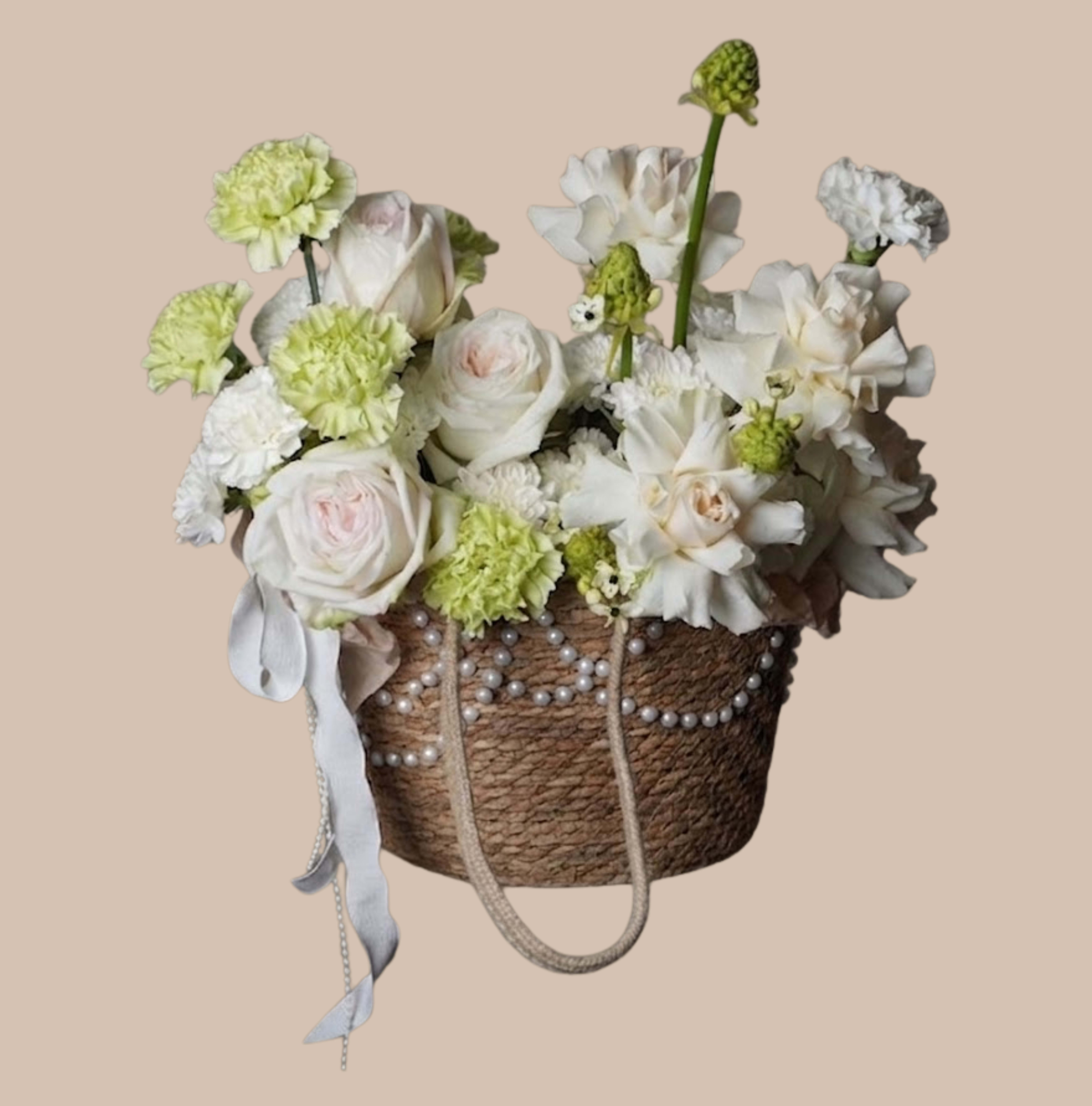 Cashmere &amp; Currant - Soft pale tones and a gentle, rounded silhouette make this flower arrangement feel like a comforting embrace - ideal as a sympathy arrangement or a calm, elegant gift for spring. The composition centers on white roses and complementary white blooms, paired with pale green carnations to create a tranquil, mixed-color palette that reads as both refined and quietly hopeful for the person you're thinking of.  Arranged in a woven basket, the blooms are gathered into an airy, abundant dome that highlights texture as much as color. A beaded, pearl-like trim and a long ribbon drape gracefully from the basket, adding rustic charm and a delicate finishing detail. The combination of roses, carnations, and soft filler flowers gives a plush, layered look that feels thoughtfully composed without being fussy.  Perfect for offering comfort, marking a gentle celebration, or brightening someone's day with understated elegance - this arrangement suits bedside tables, mantels, or entryway displays. The basket presentation arrives ready to place; for best longevity, replace water daily and trim stems if transferring to a vase.