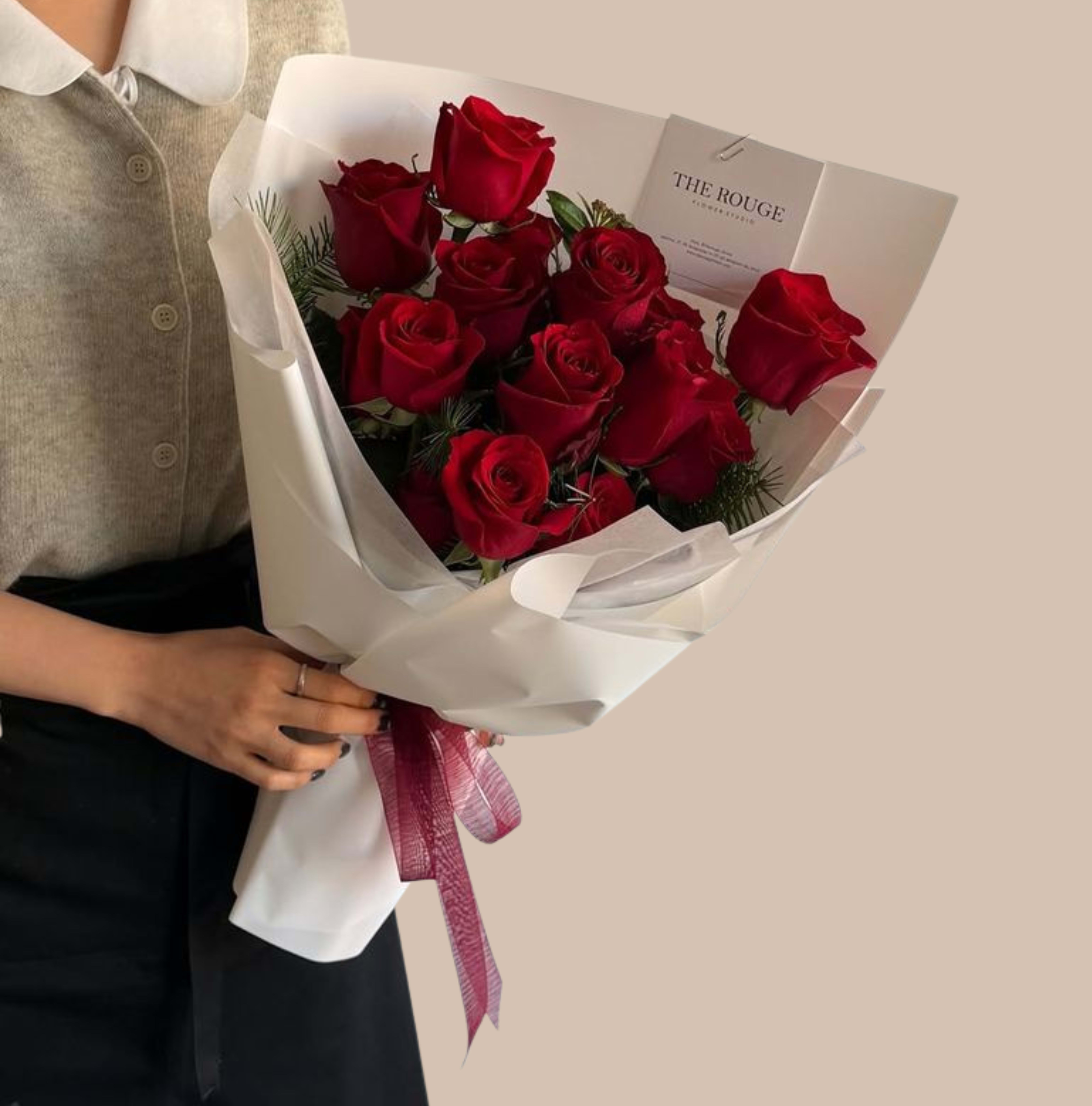 Rouge &amp; Wrapped - A compact cluster of deep red roses delivers an immediate impression of classic romance - the perfect love and romance bouquet to make someone feel cherished. The saturated crimson blooms sit tightly gathered for an intimate, luxurious look, while the pale white paper wrap and soft pink ribbon add a refined, modern contrast that keeps the arrangement feeling fresh and gift-ready.  This wrapped floral arrangement features richly colored roses accented only by the crisp white paper and a delicate pink bow, creating a focused, elegant composition. A printed card is tucked into the bouquet for a personal note; the finished package reads as thoughtful and polished without extra fuss. Dimensions are that of a handheld wrap - easy to carry and present - and the structure keeps stems secure so the recipient can enjoy the visual impact right away.  Ideal for anniversaries, Valentine's moments, or any day you want the person you're thinking of to feel truly seen and adored, this bouquet arrives ready to hand over and admire. For best enjoyment, keep blooms in fresh water and out of direct heat; if you'd like a longer-lasting display, ask about vase options or same-day delivery to ensure peak freshness.