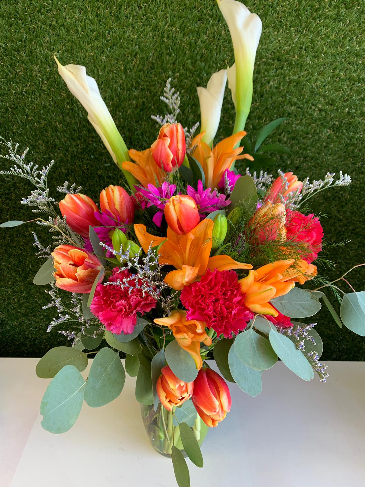 Bright mixed bouquet with calla lilies, tulips, carnations, and lilies in a glass vase