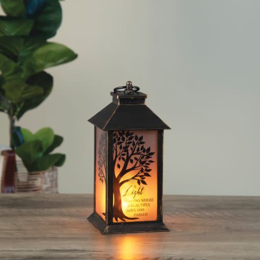 Timeless Tribute Beautiful Soul Lantern  - A quiet, comforting memorial lantern designed to honor a loved one with gentle light and thoughtful symbolism-perfect for a sympathy arrangement or tabletop remembrance. This memorial lantern brings a solemn, reflective presence to a home or funeral tribute, offering the kind of calm warmth that helps the person you're remembering feel peacefully honored.  The compact weathered bronze lantern features frosted panels that diffuse a warm amber glow and a front panel etched with a tree silhouette and remembrance text, creating a simple yet meaningful focal point. Its dark, understated finish and small footprint make it suitable for mantelpieces, bedside tables, or a memorial display; no ornate details, just a dignified design that lets the light and message speak.  Offer this as a sympathy gift to convey heartfelt condolences and steady comfort during a difficult time-the kind of keepsake that invites quiet reflection. Sized for tabletop use and ready to place where it can be seen and felt, and a lasting reminder of care and remembrance.