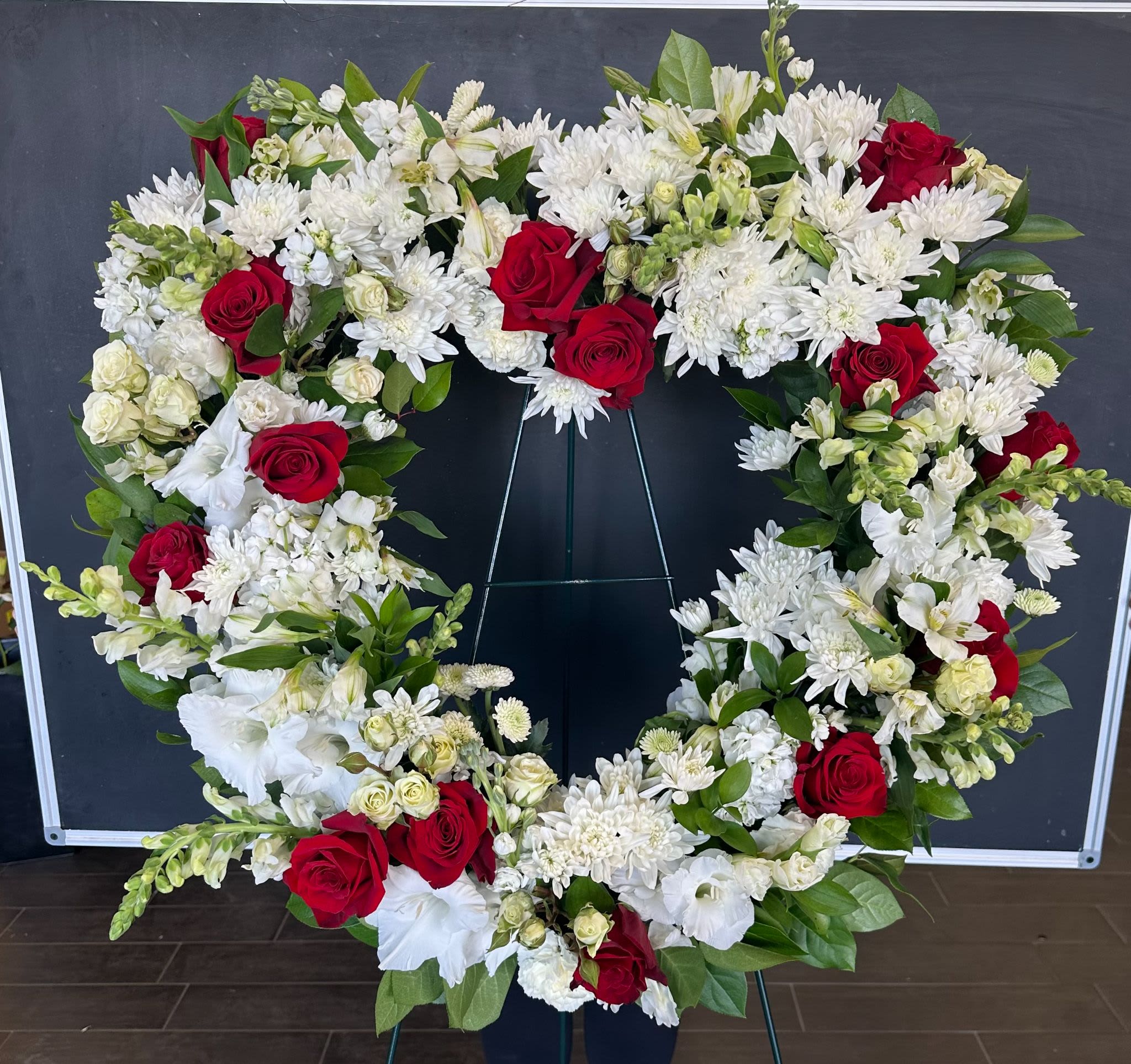 Heart-shaped floral wreath with red roses and white flowers on a stand