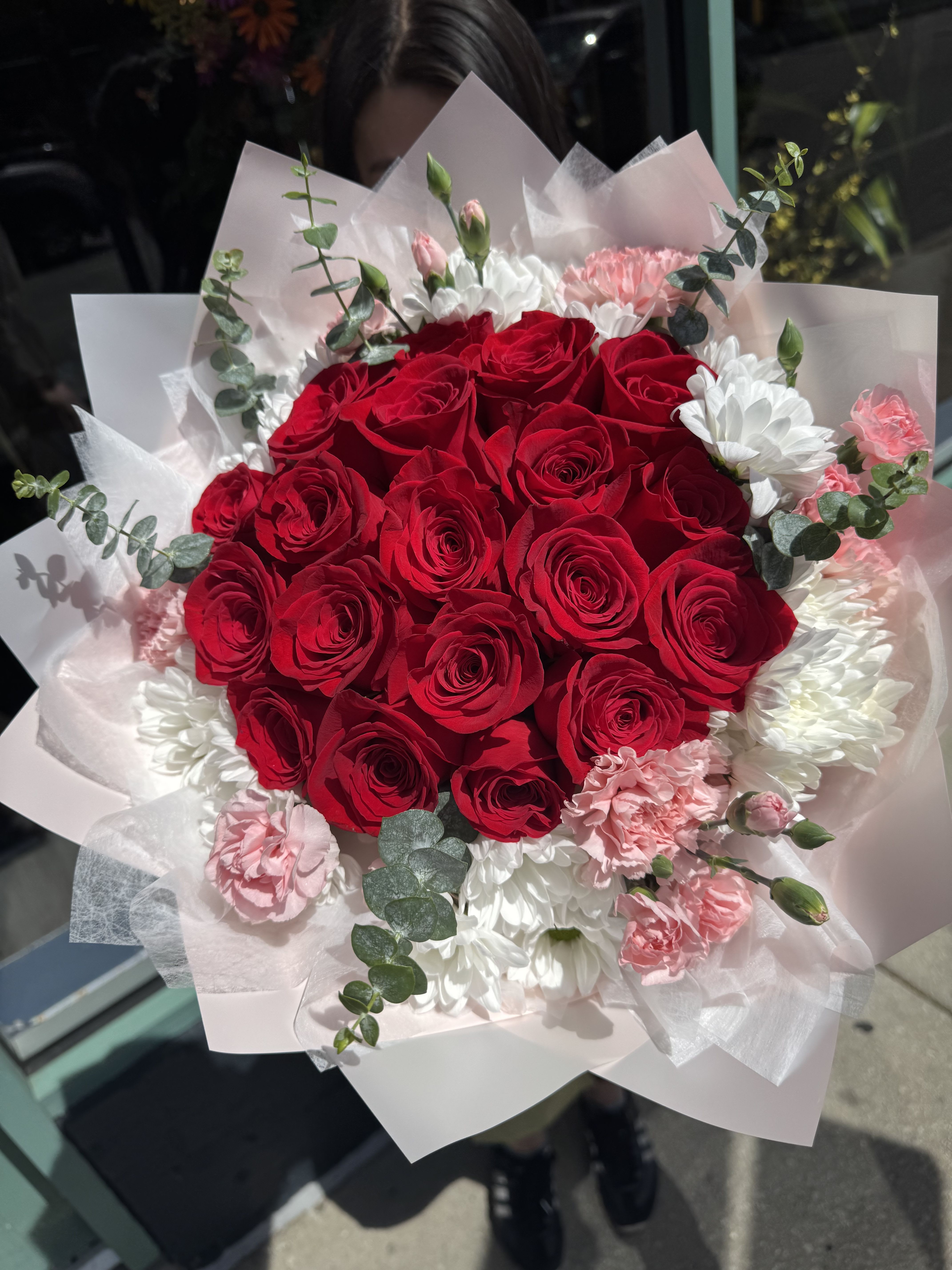 Blooming with love  - A dense cluster of vivid red roses takes center stage in this romantic hand-tied bouquet, making it an ideal birthday bouquet or anniversary roses gift that reads as both passionate and celebratory. Soft pink carnations and crisp white daisies cradle the roses, so the person you're thinking of will feel truly cherished the moment they see the rich red and rosy-pink contrast against fresh green eucalyptus accents.  Wrapped in pale pink and white tissue with floral wrap for an elegant presentation, the arrangement has a lush, full shape that suits love-themed occasions or any special personal celebration. The eucalyptus adds a light, airy texture and soft scent while the mix of roses, chrysanthemums, and carnations creates long-lasting color and presence - perfect for making someone feel seen and adored.