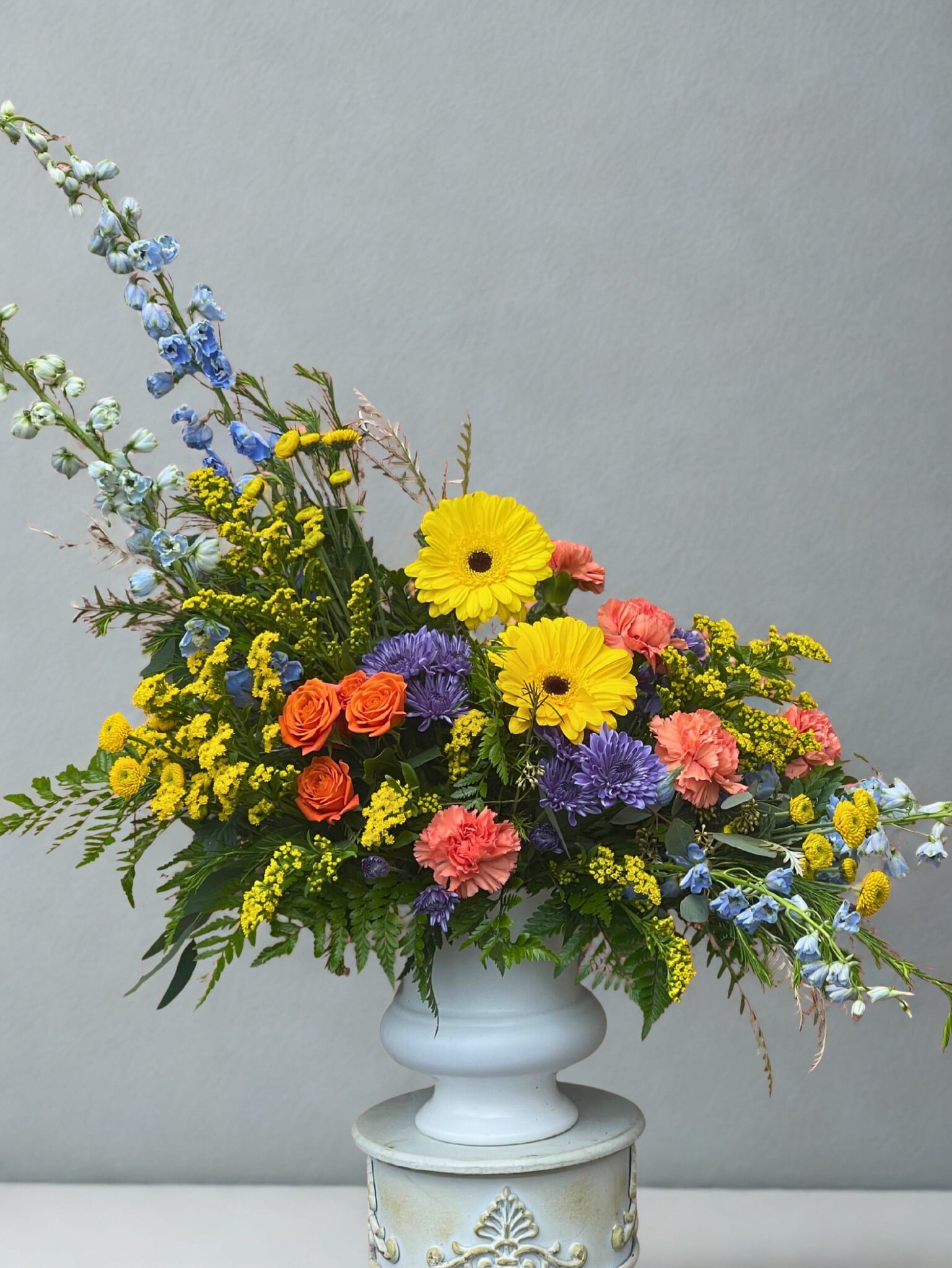 Colorful mixed flower arrangement in a white pedestal vase