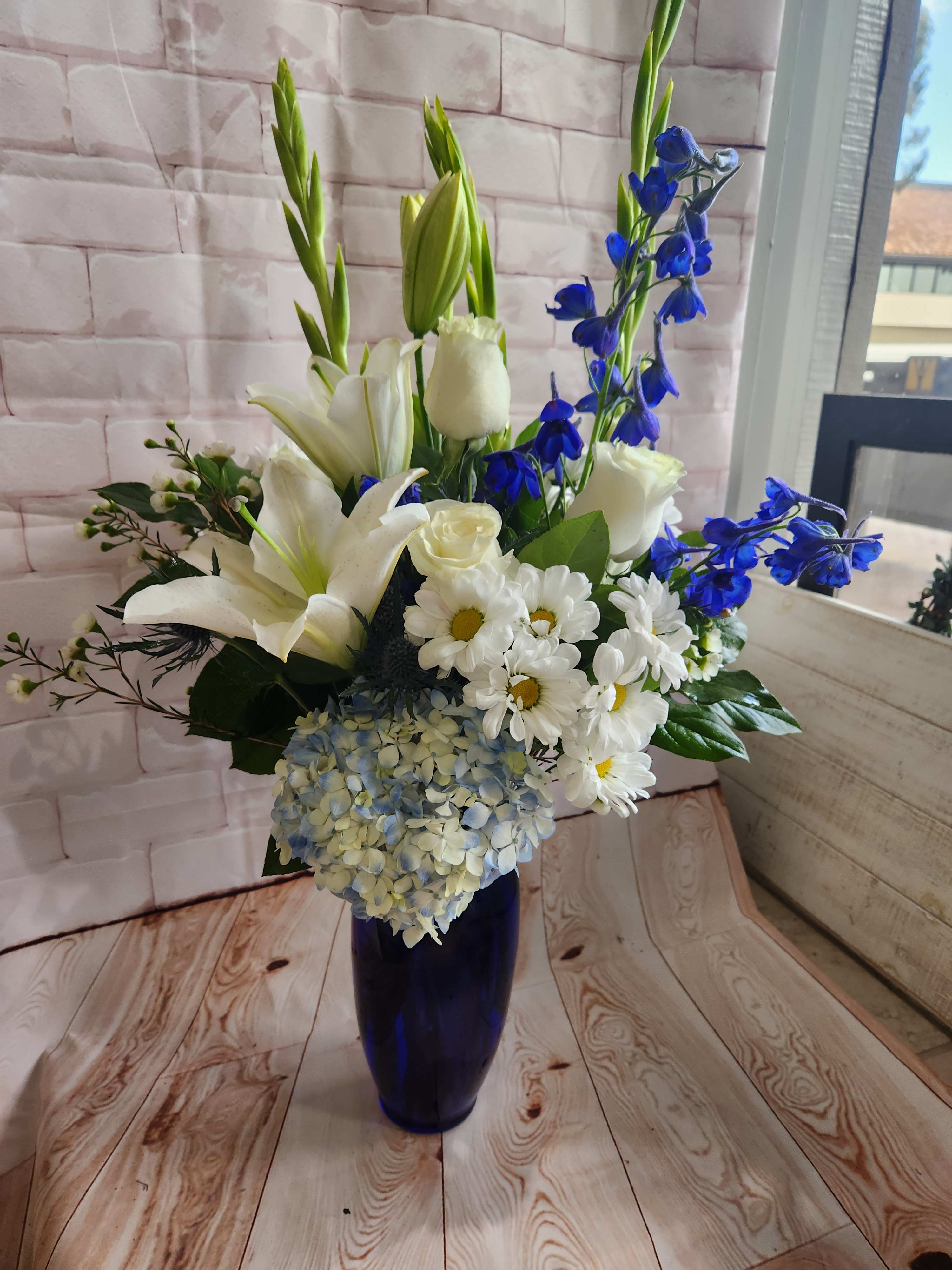 White lilies, roses, daisies, and blue flowers in a dark blue vase